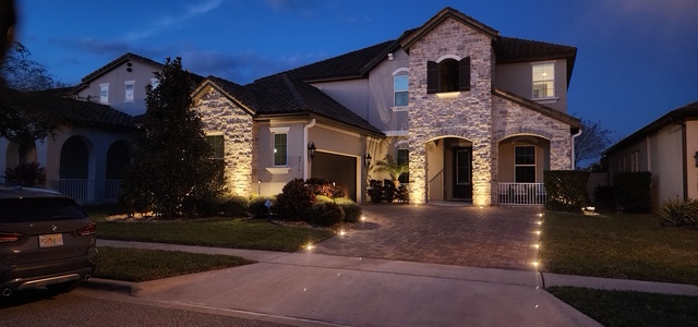 A two-story stone house at dusk, illuminated by glowing landscaping lights along the driveway and facade. A two-story stone house at dusk, illuminated by glowing landscaping lights along the driveway and facade.