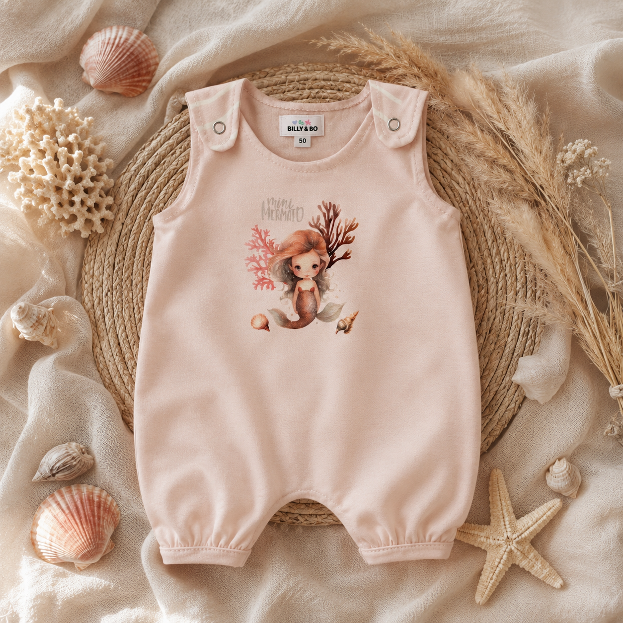 De baby ligt op een zachte beige deken, gekleed in een roze romper met hertenprint.