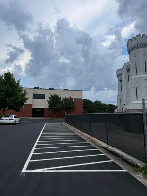 Parking lot beside a white stone castle-like building under cloudy skies, with a red building and parked car nearby.
