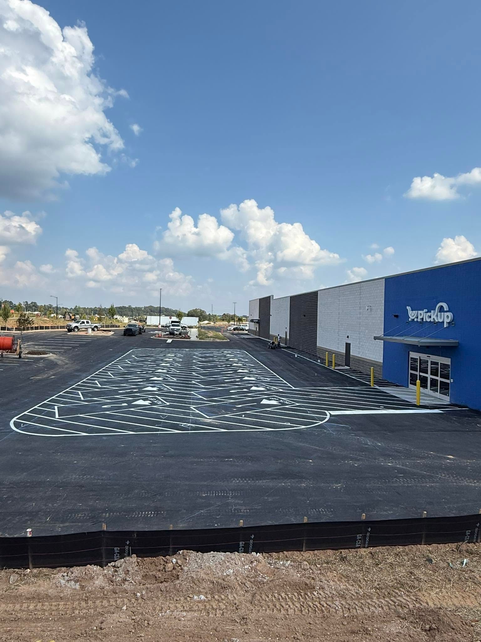 Outdoor construction lot with black surface, white markings, and a blue building under a clear sky