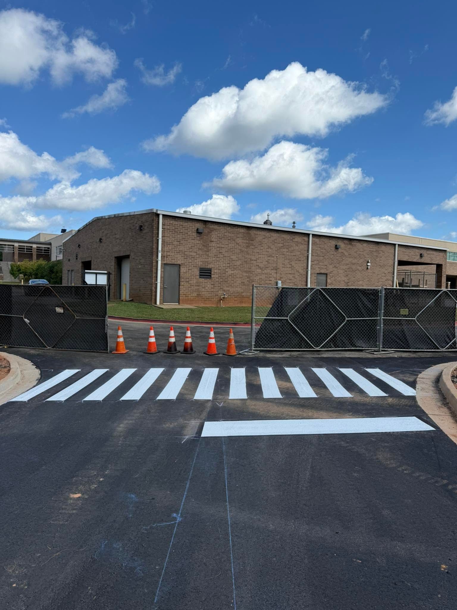 Crosswalk leading to a brick building under a blue sky, with orange cones blocking the entrance.