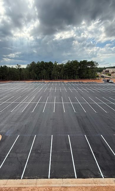 Empty parking lot with white lines under a cloudy sky, bordered by trees.