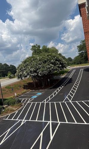 Empty parking lot with white striped pavement, a large tree, and cloudy sky beside a brick building