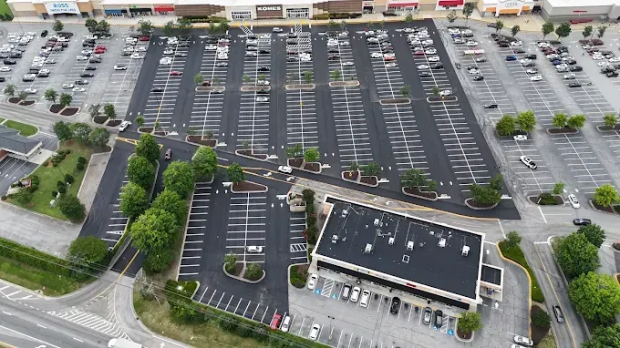 Aerial view of a large, mostly empty parking lot beside a commercial building with a few cars and landscaped islands