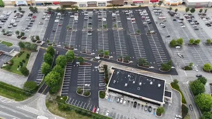 Aerial view of a large, mostly empty parking lot beside a commercial building with a few cars and landscaped islands