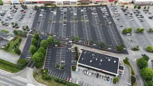 Aerial view of a large, mostly empty parking lot beside a commercial building with a few cars and landscaped islands