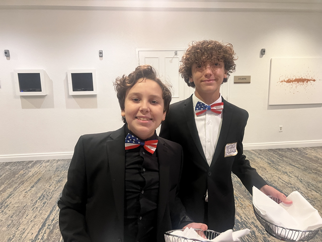 Two young boys in suits and bow ties are posing for a picture