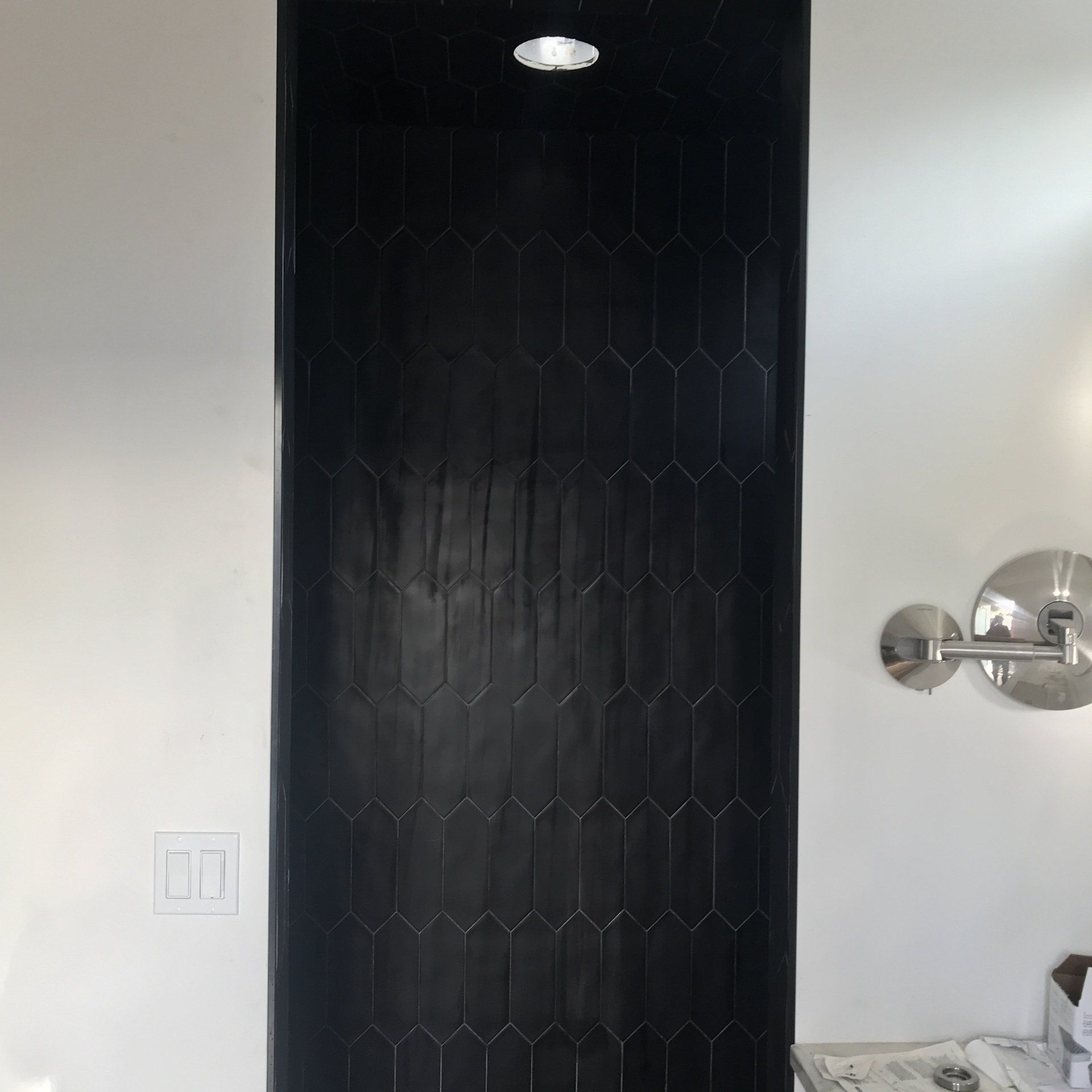 Black tiled wall between white walls, with a light fixture and chrome sconce.