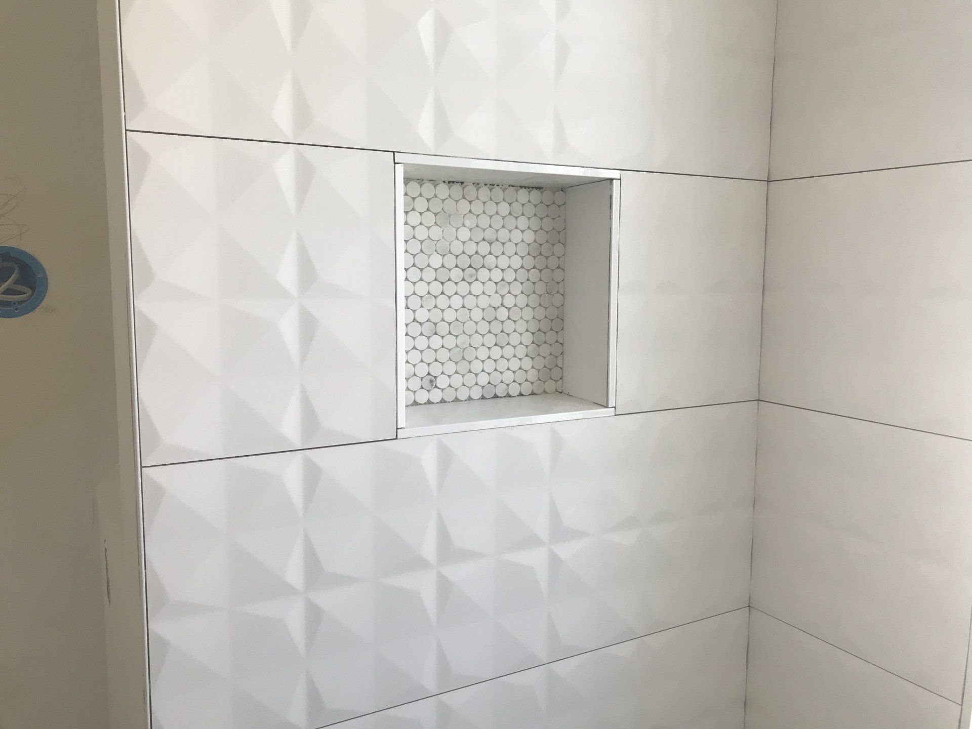 White tiled shower with a built-in niche lined with small mosaic tiles.