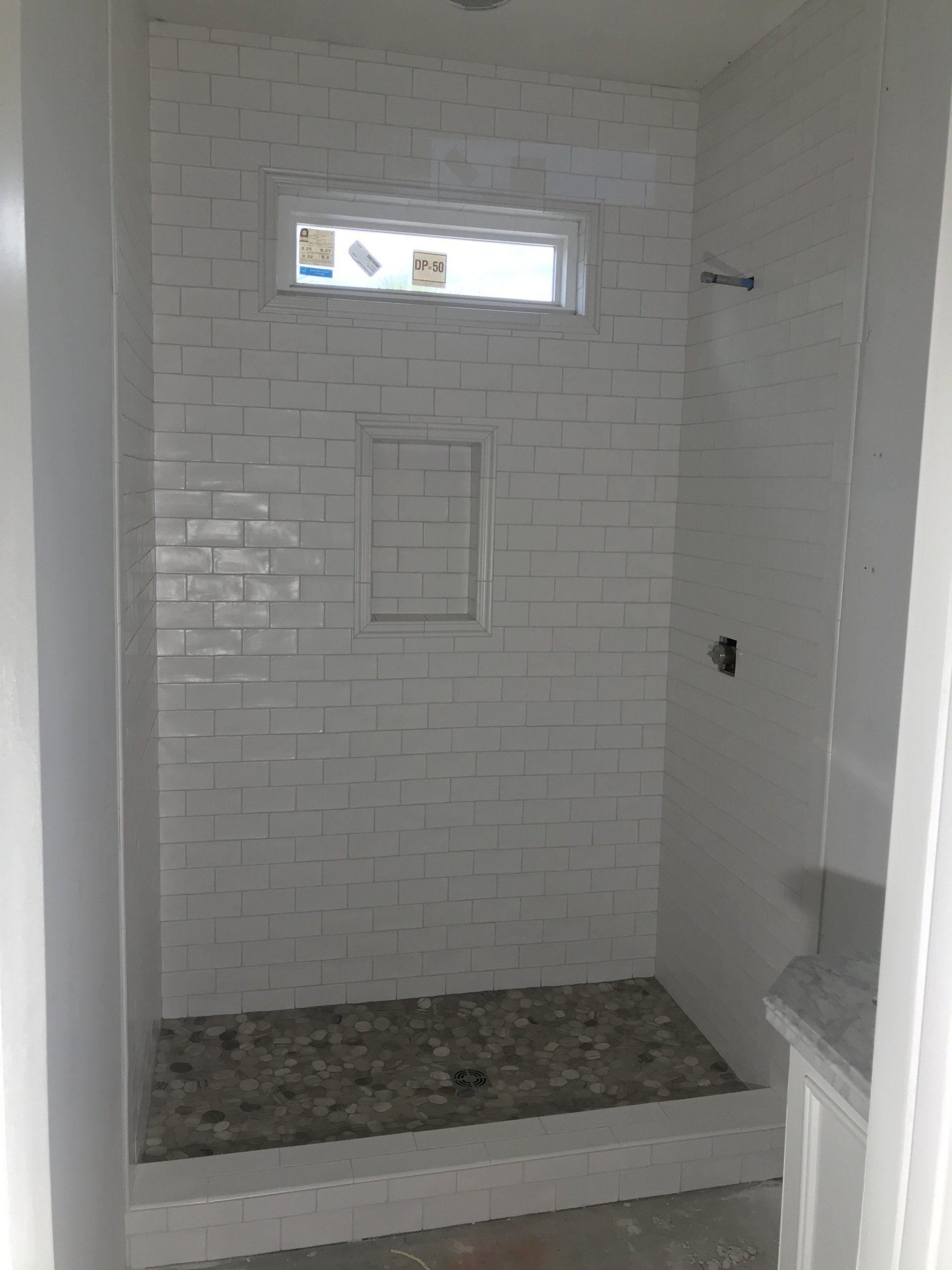 White tiled shower with pebble floor, recessed shelf, and small window.