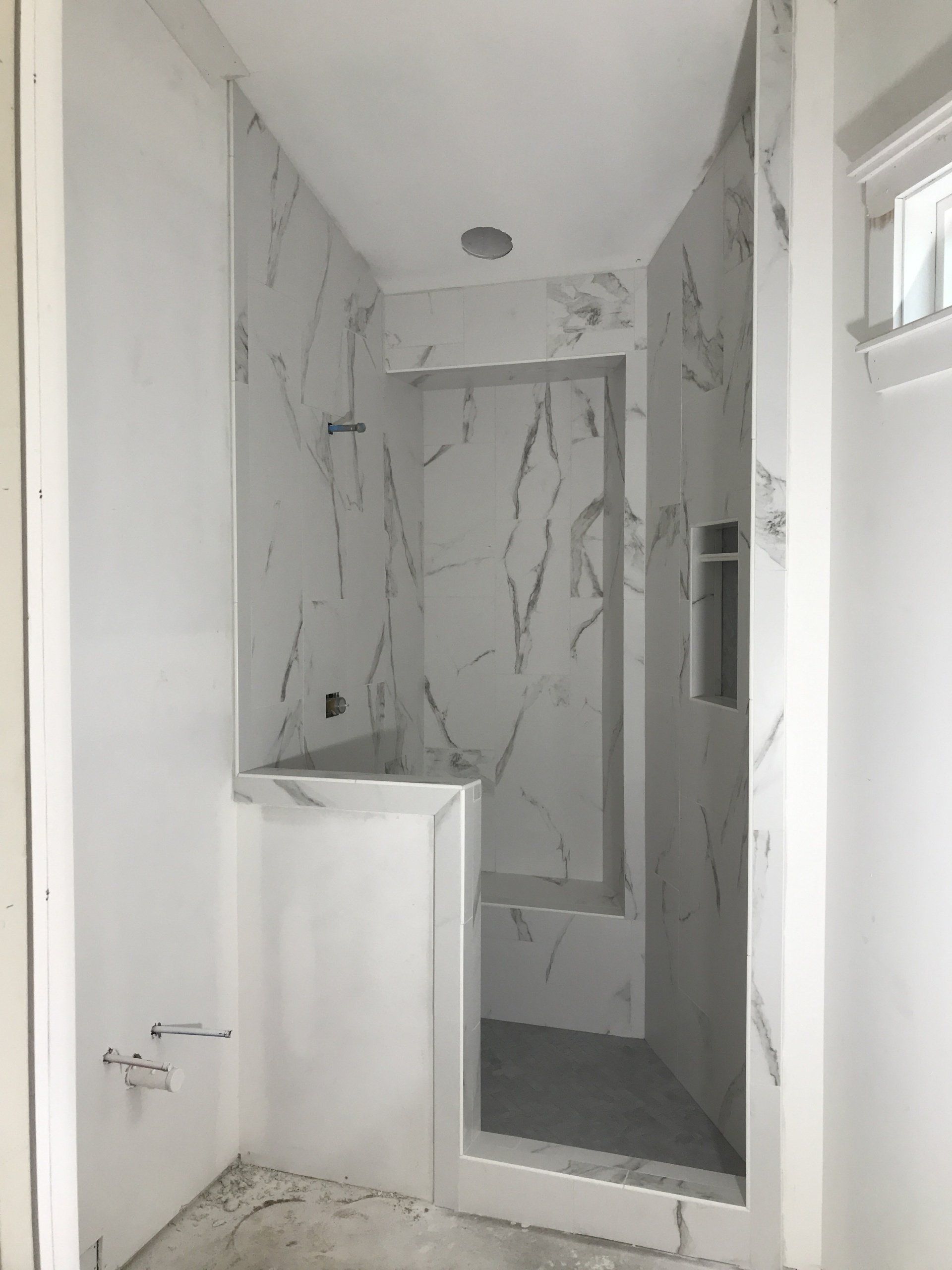 A newly tiled, marble-look shower stall in a light-filled bathroom, showing construction progress.