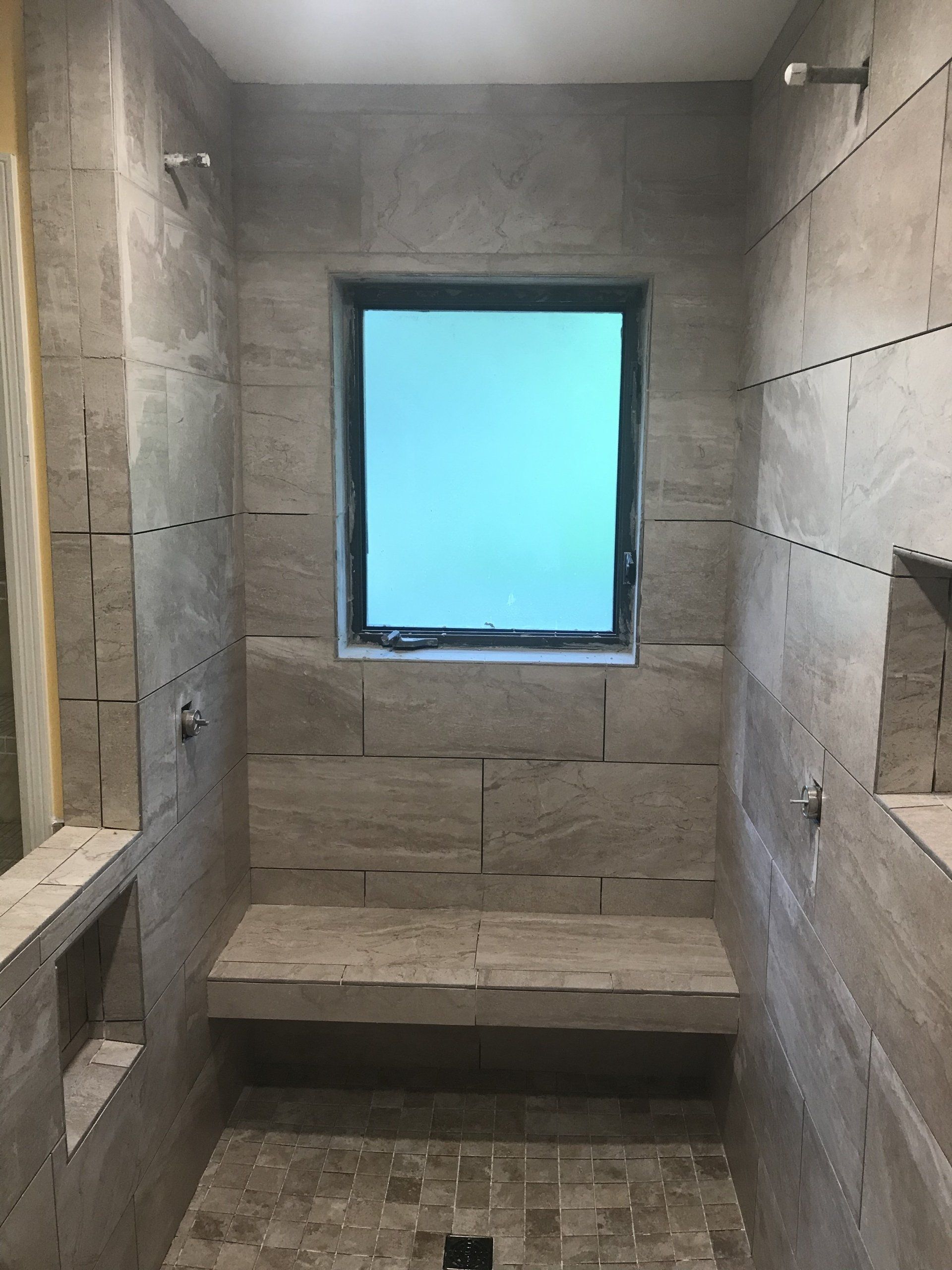 Shower with stone tile walls, built-in bench, window, and two shower heads.