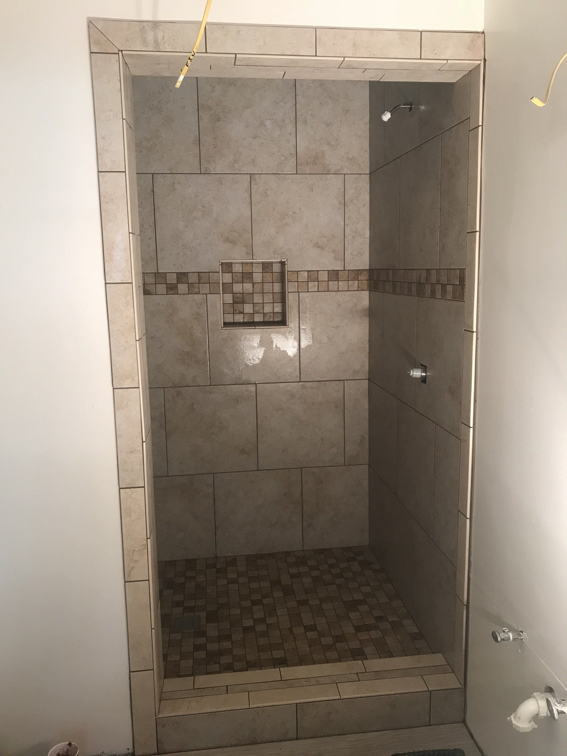 Tiled shower stall with stone floor and built-in bench. Beige tiles with dark accent tiles.