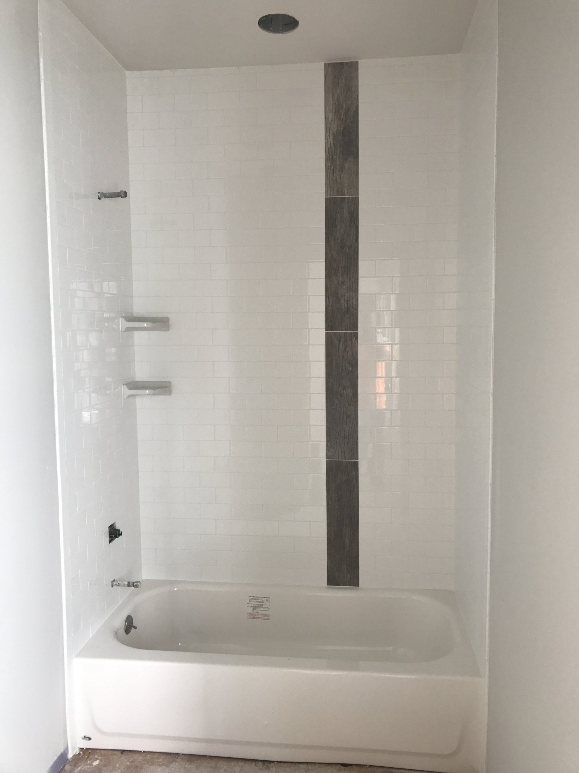 White tiled shower with a dark gray strip, a white tub, and silver shower fixtures.