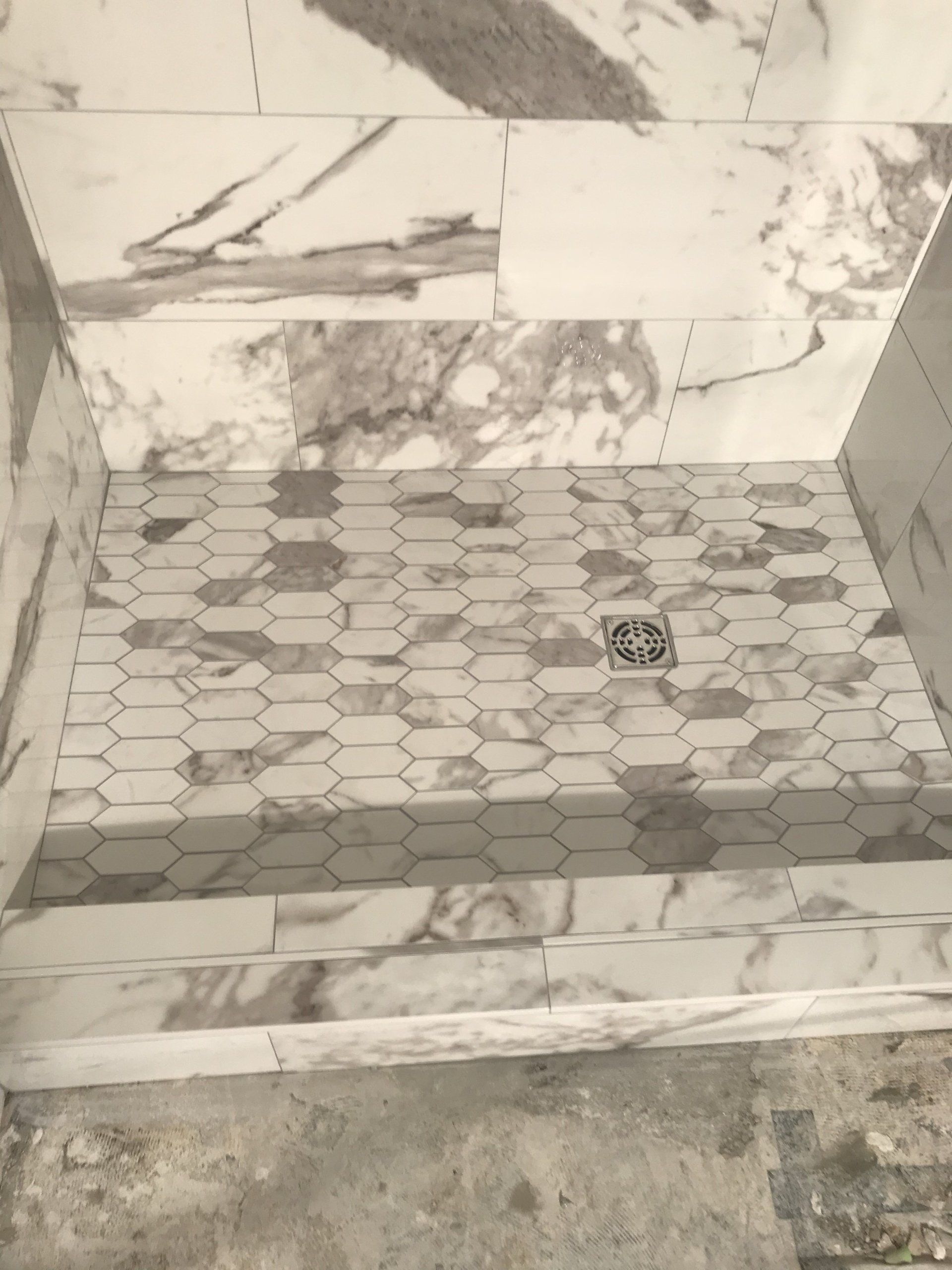 Shower with marble-patterned walls and honeycomb floor tiling, centered around a drain.