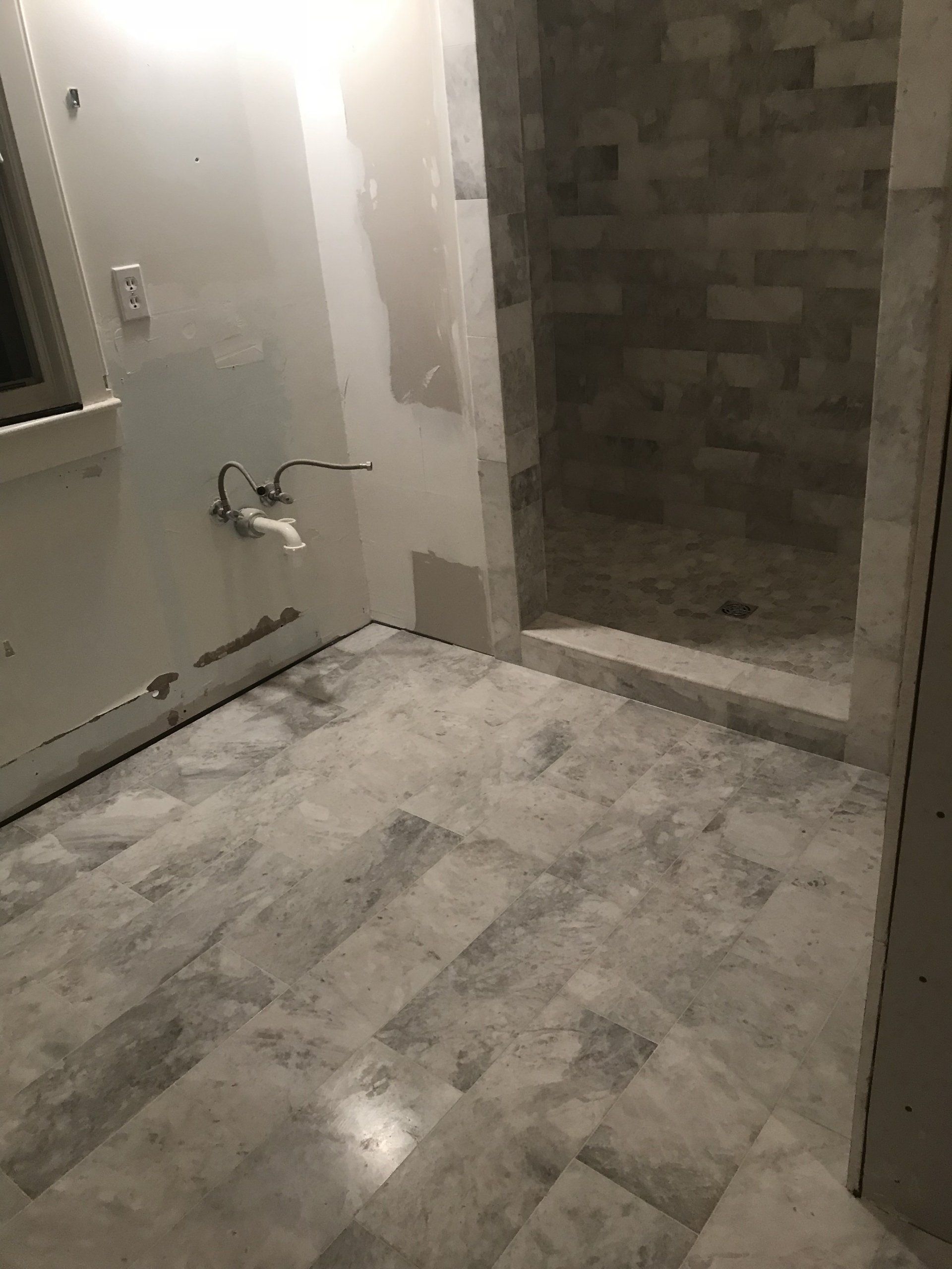 Bathroom under construction with gray tile floor, shower stall, and exposed plumbing.