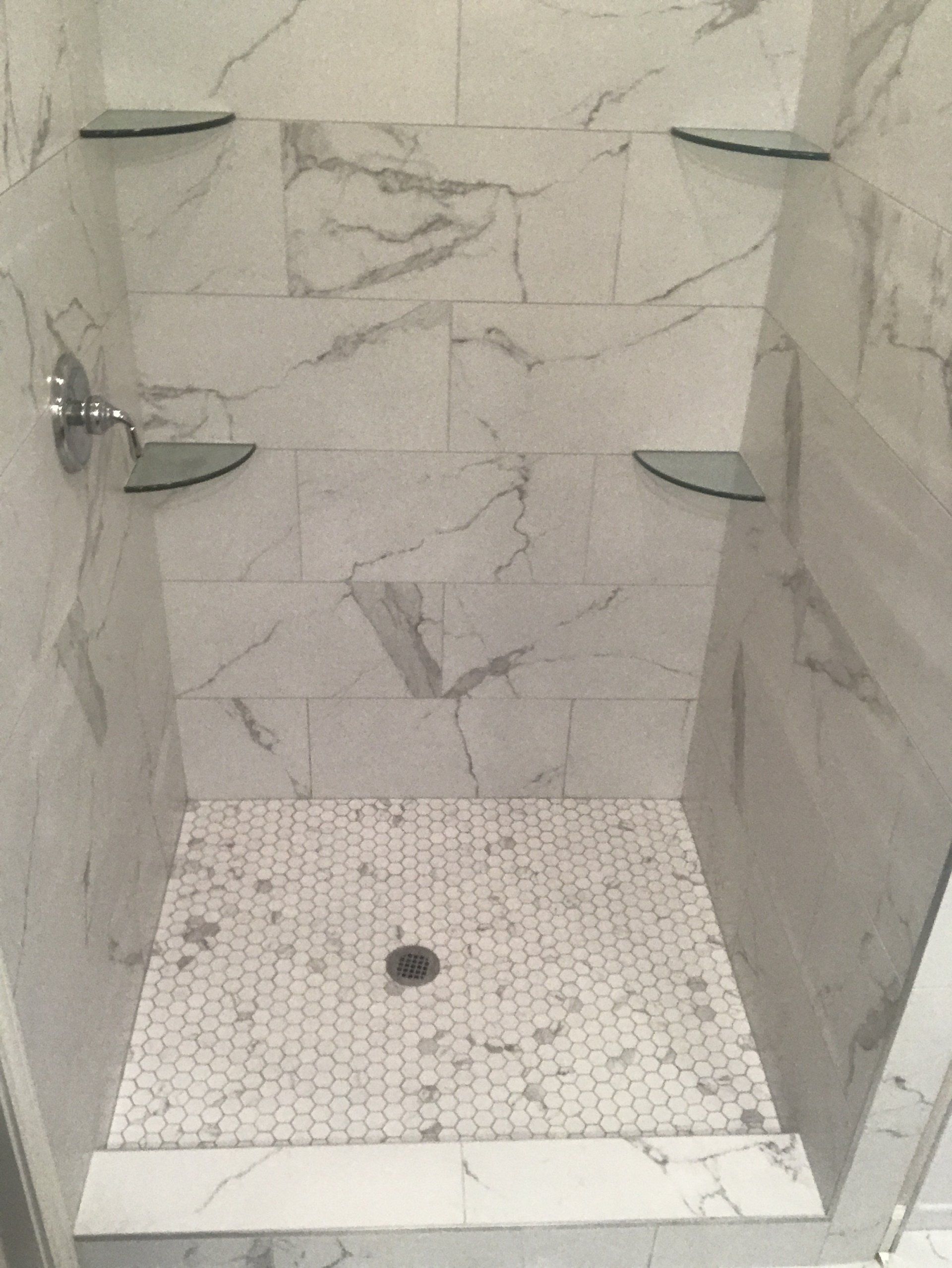 Shower stall with marble-patterned tile, glass shelves, and a mosaic tile floor.