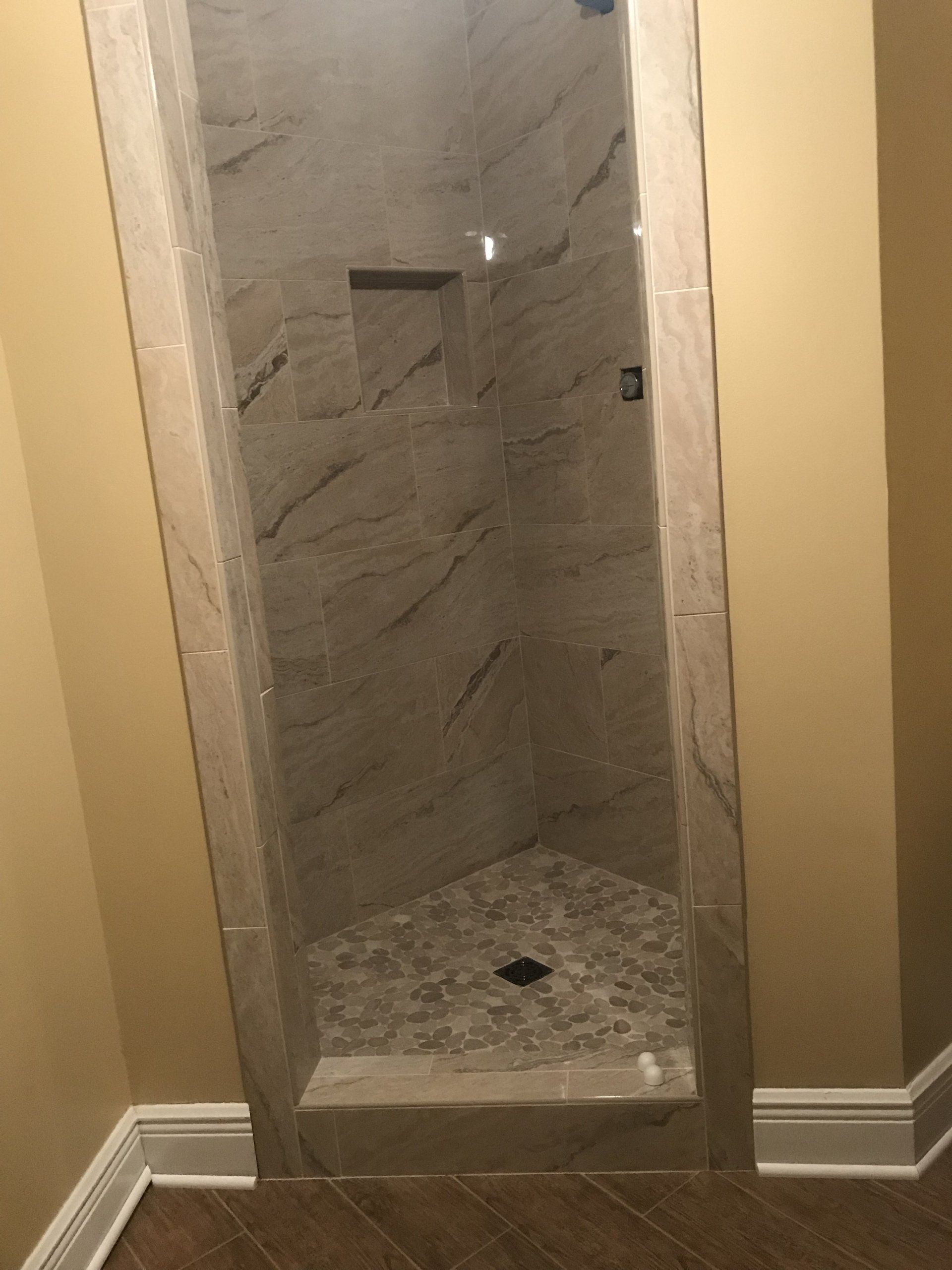 A tiled, walk-in shower with stone floor and built-in niche. Beige walls, beige tile, and a step up.