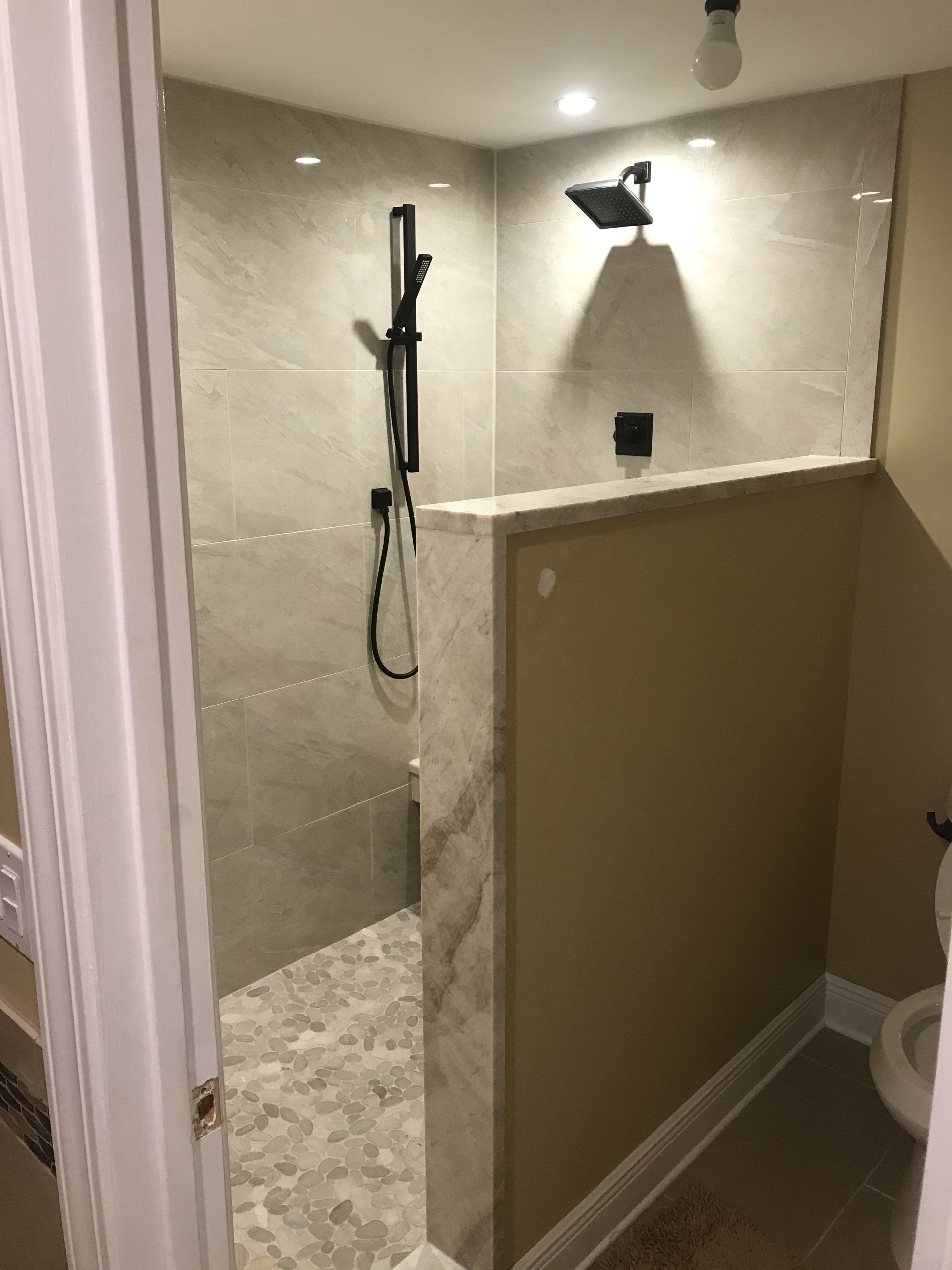 Shower stall with beige tile, black shower fixtures, and a partially open entry.