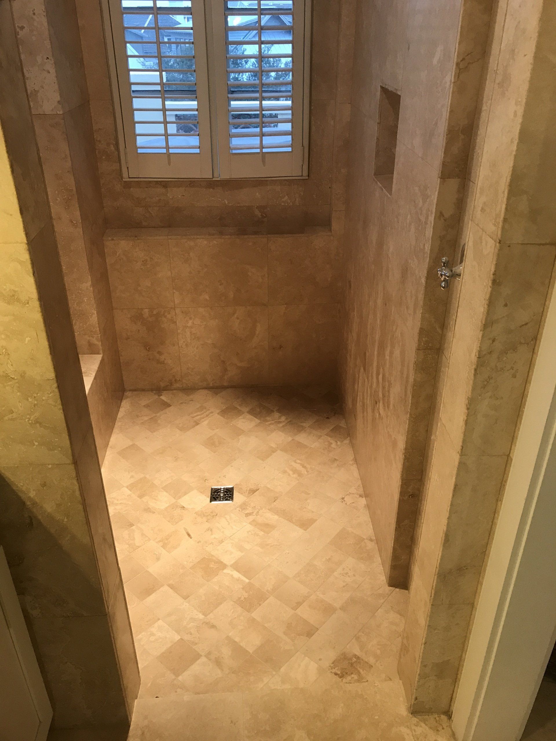 Beige tile shower with window, built-in bench, and drain.
