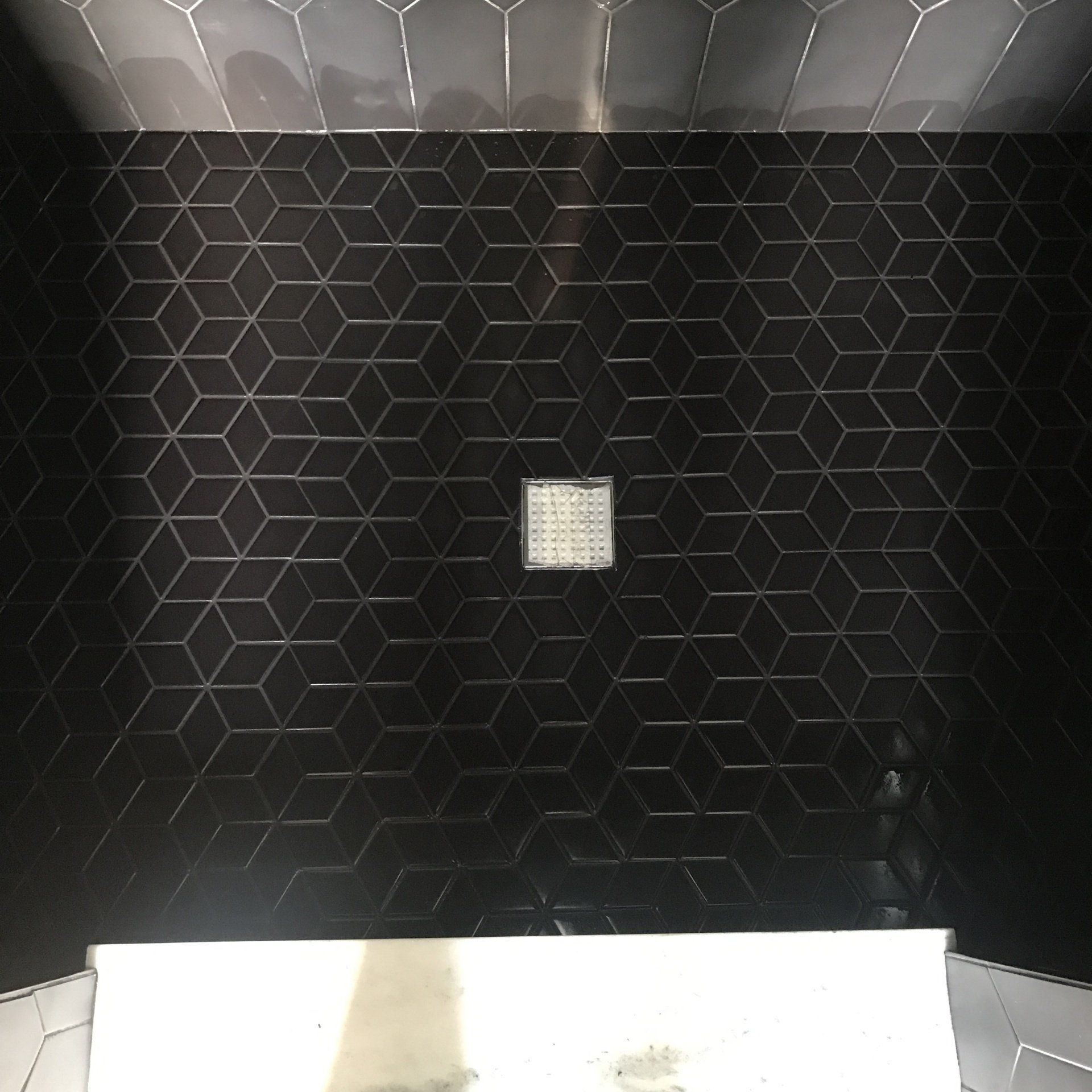 Black geometric tiled shower with a drain.