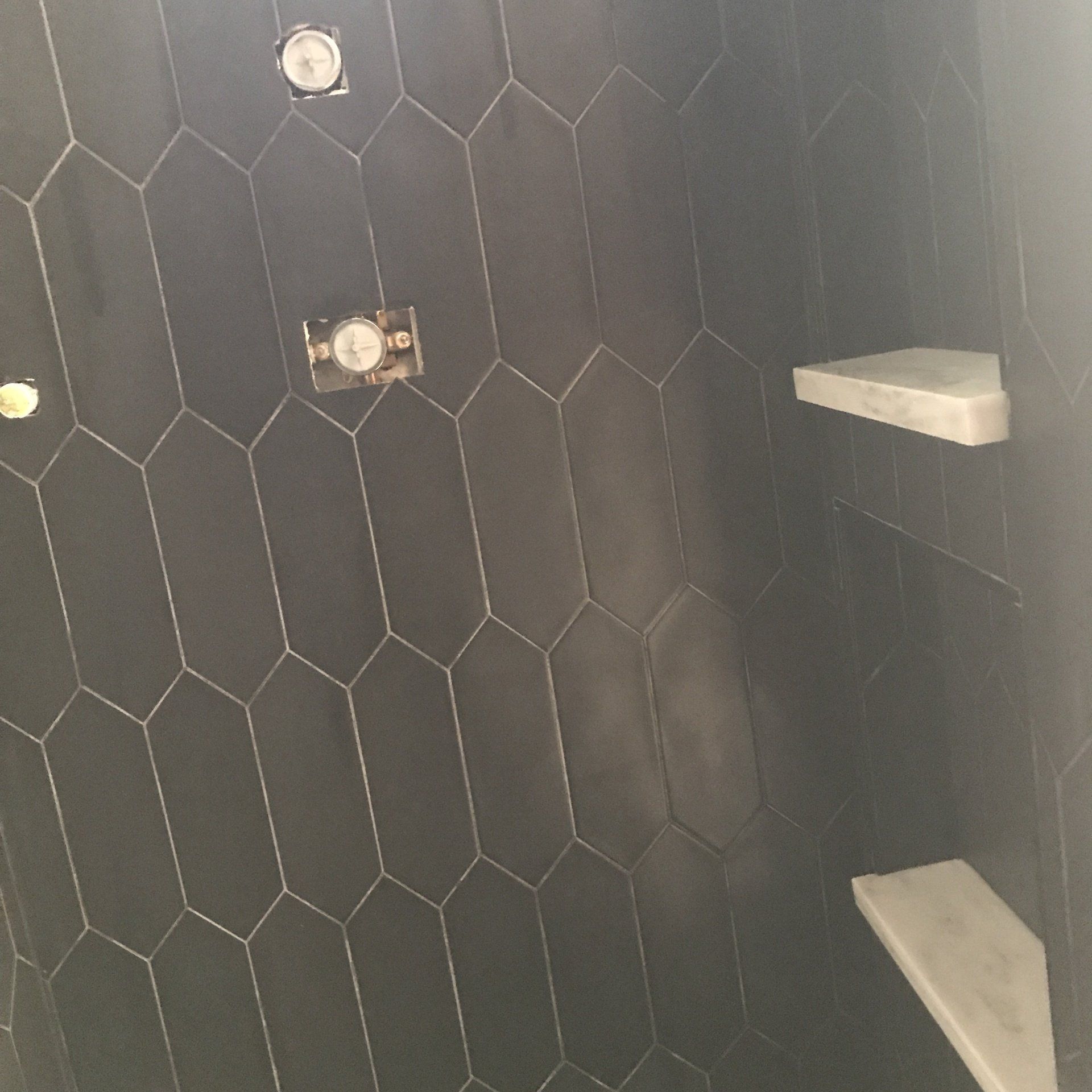 Black tiled shower with grey shelves and shower fixtures.