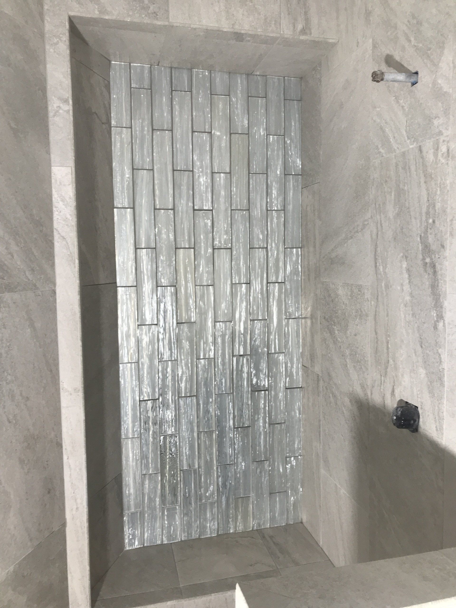 Shower niche with gray tiles and textured, vertically-laid glass tiles.