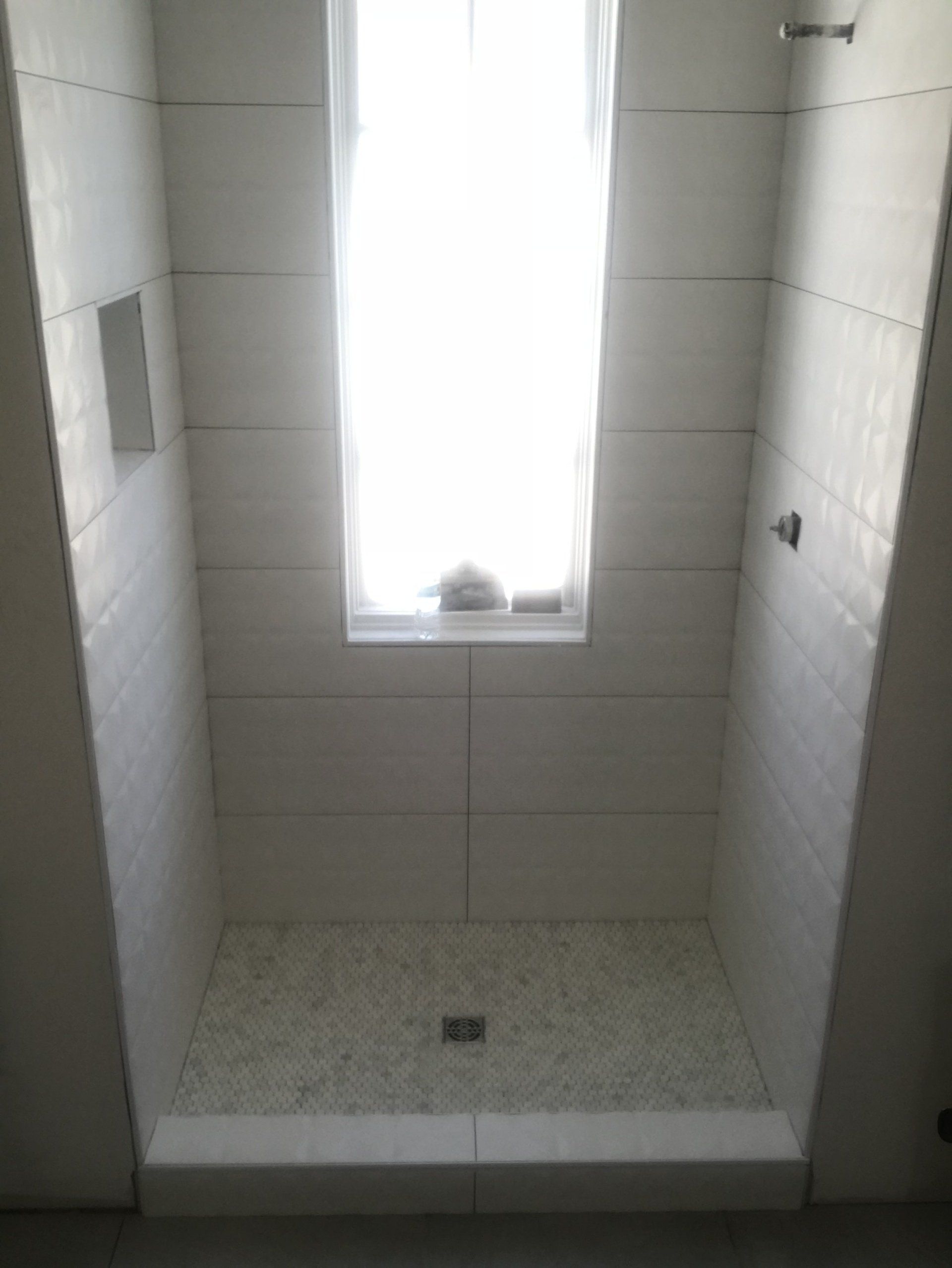 White tiled shower with a pebble-tiled floor, a window in the back wall, and a built-in shelf.