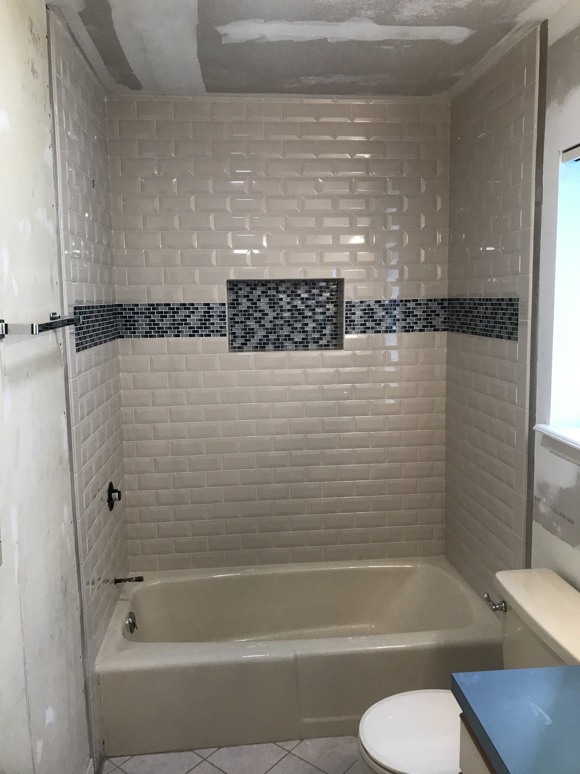 Bathroom with beige subway tiles, a black and blue mosaic accent, and a white bathtub.