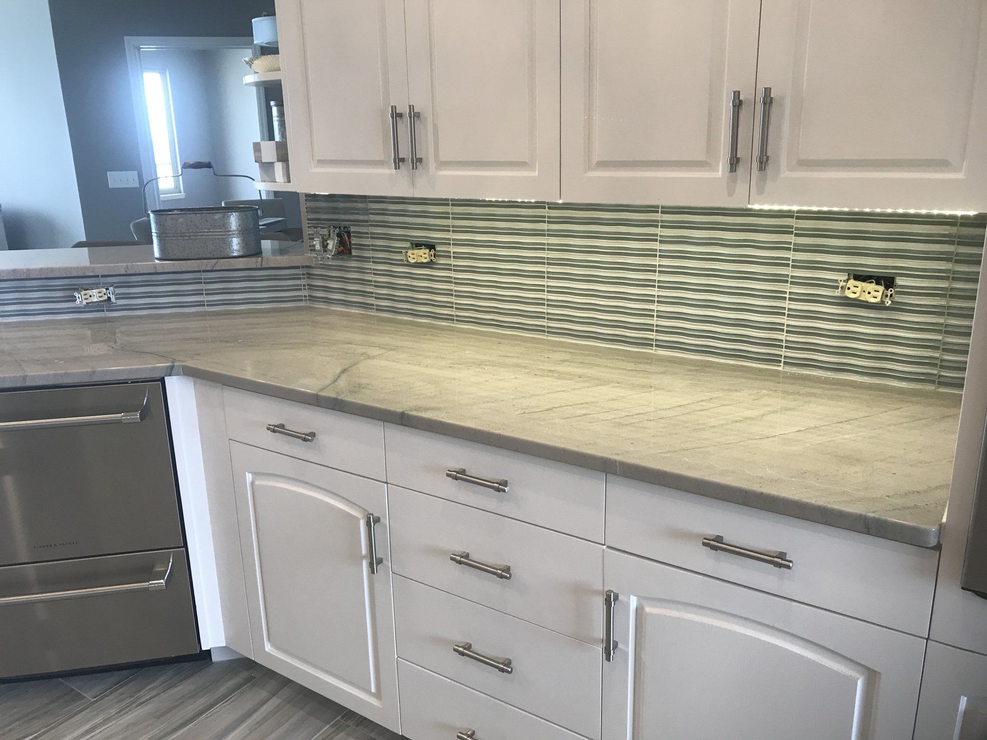 White kitchen cabinets with light countertops and a green patterned tile backsplash.