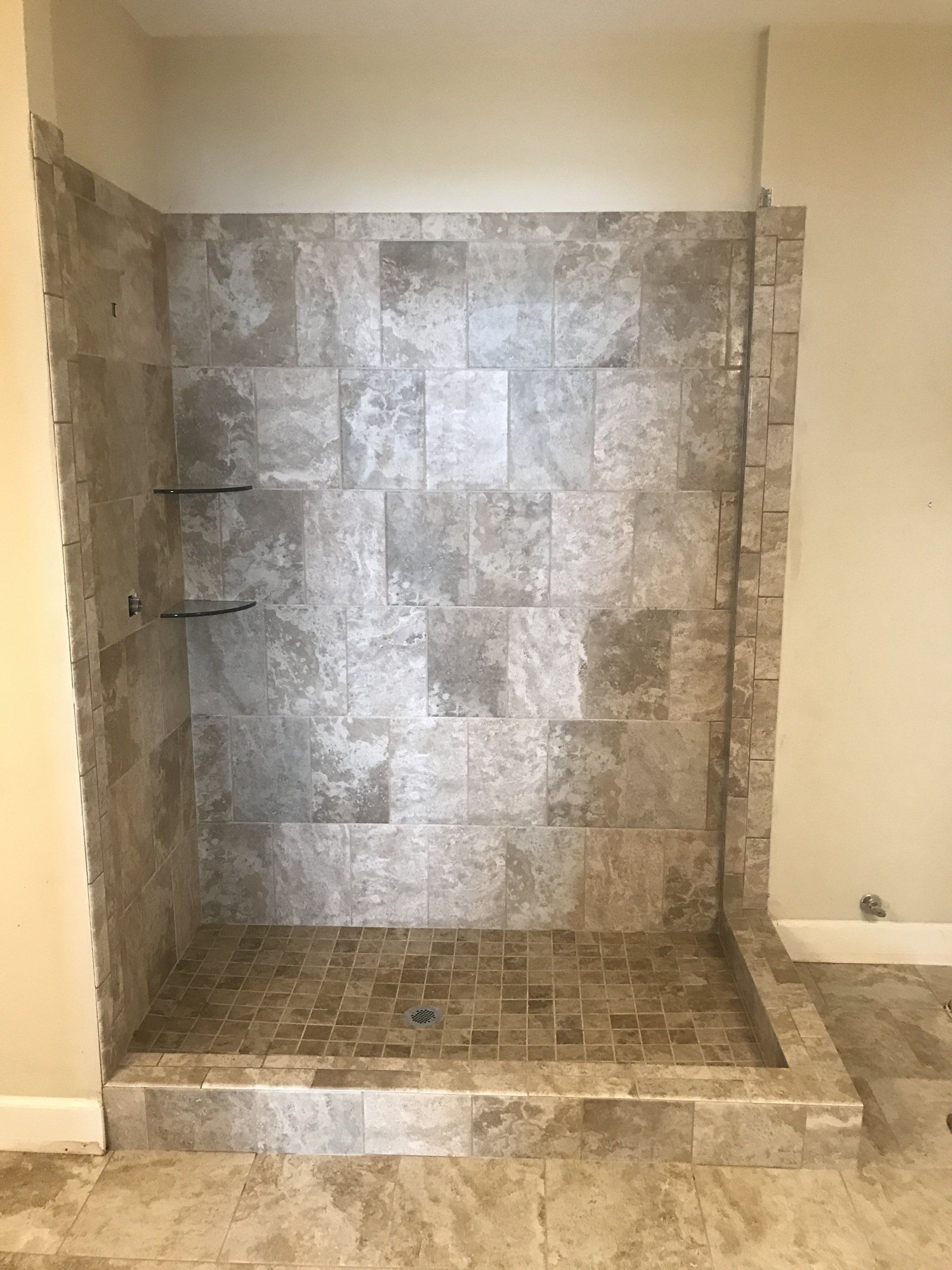 Shower stall with gray tile walls, built-in shelves, and a tiled base under construction.