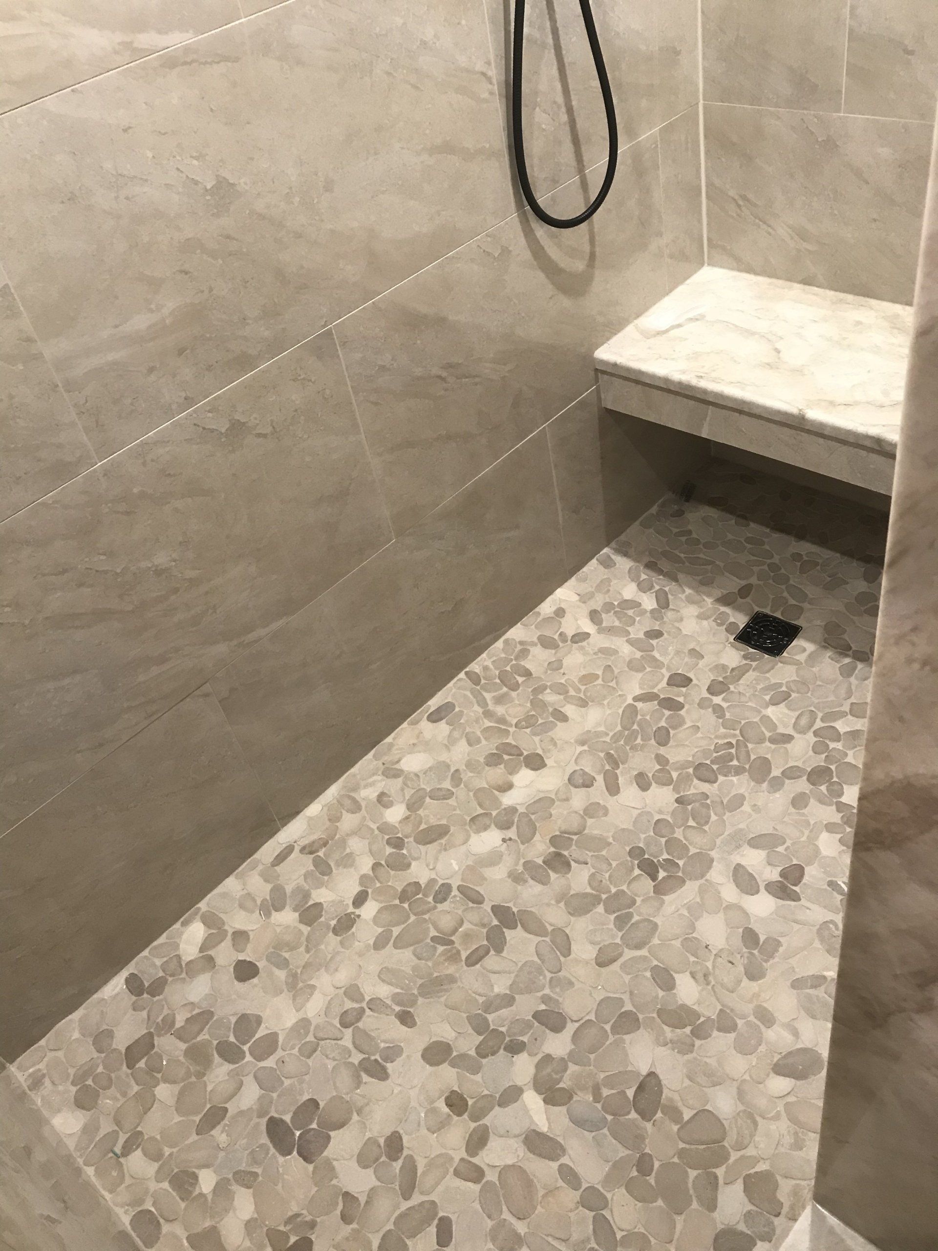 Shower stall with pebble floor, beige tile walls, and a built-in bench.