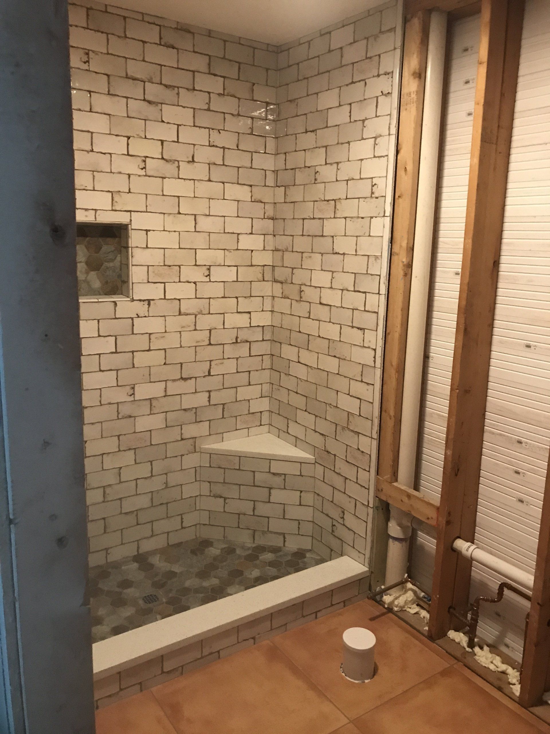 Shower in progress: white tiled walls with built-in bench and recessed niche. Open wall frame visible.