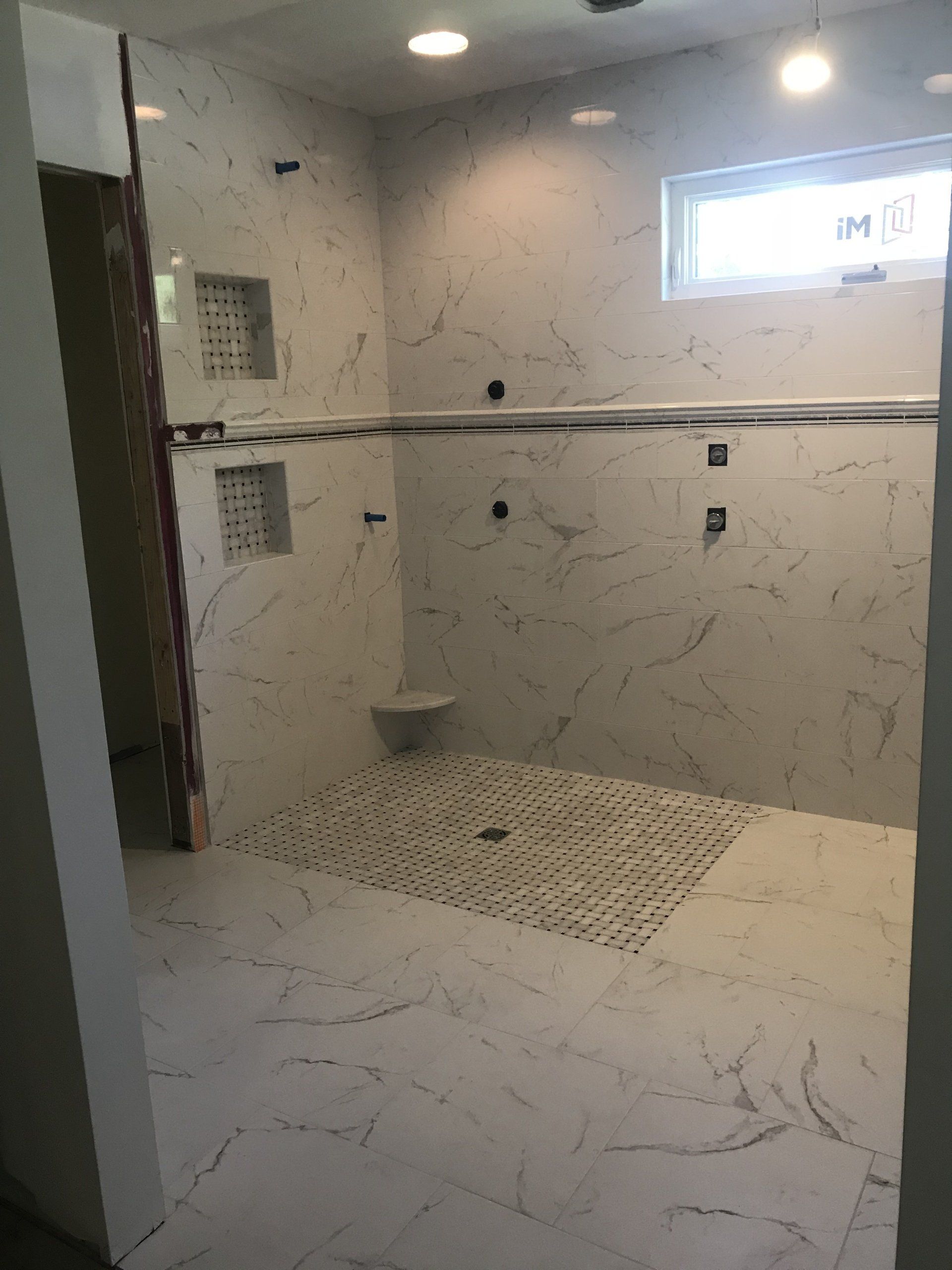 Newly tiled bathroom with white marble-look walls, built-in shelving, and dark-tiled shower floor.