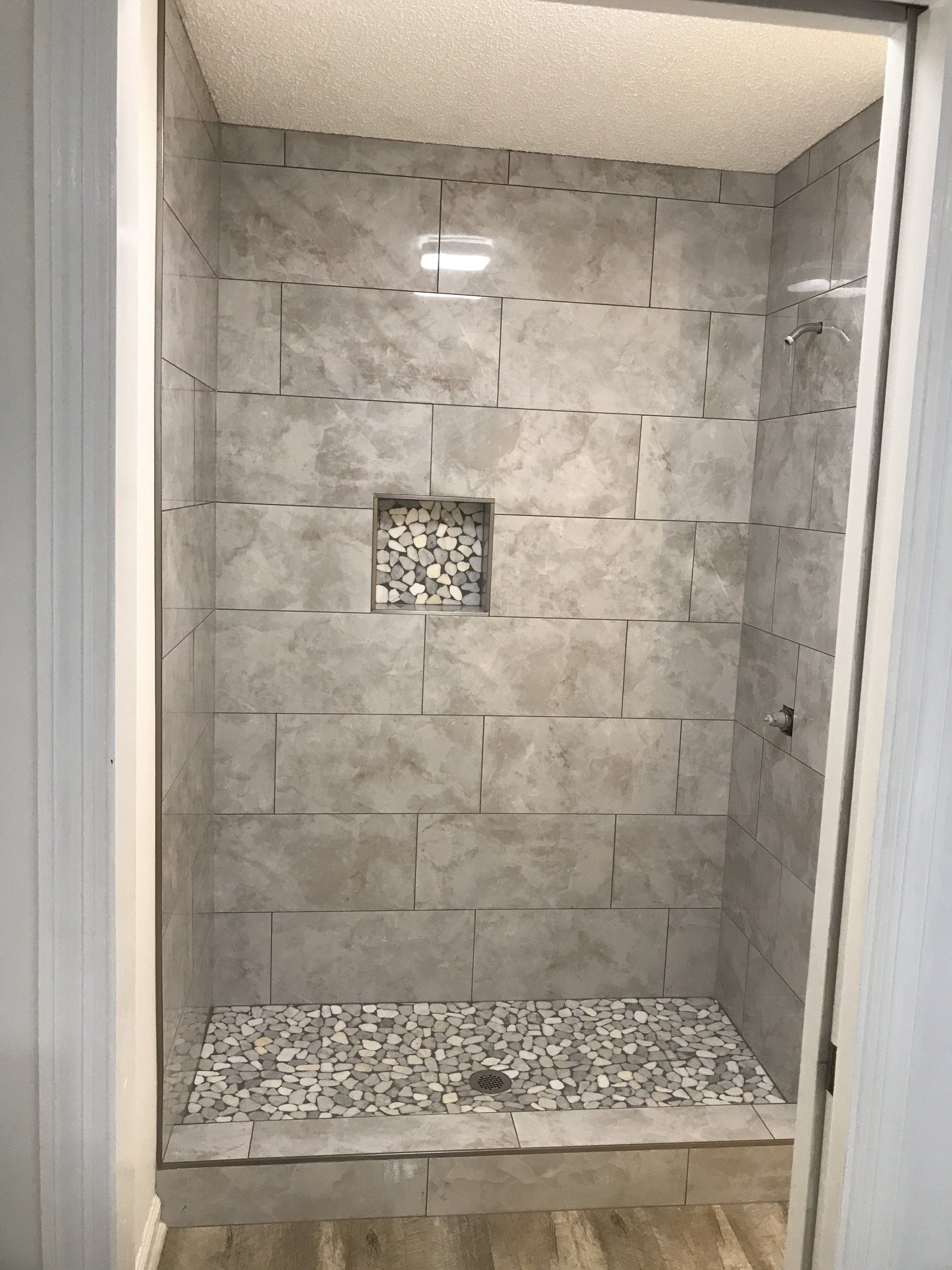 Gray tiled shower with pebble floor, niche, and recessed lighting.