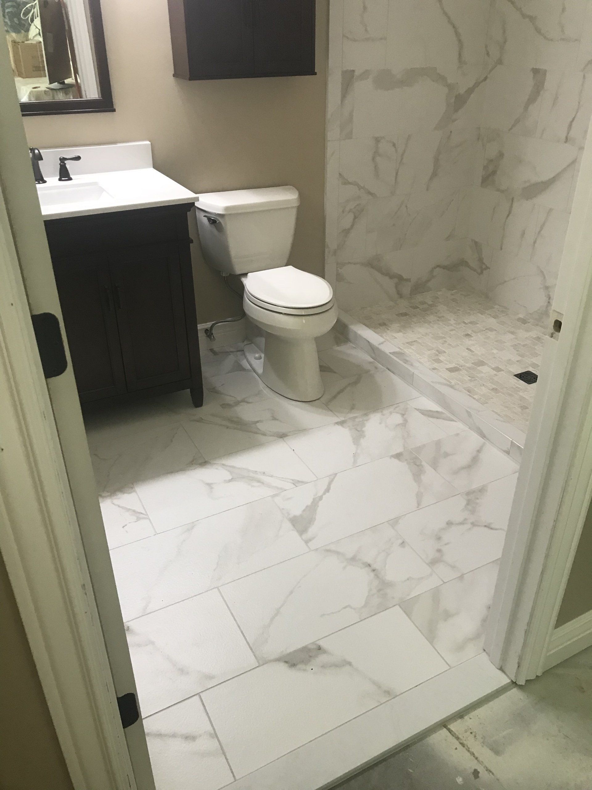 Bathroom with white marble tile floor and shower, dark vanity, and toilet.