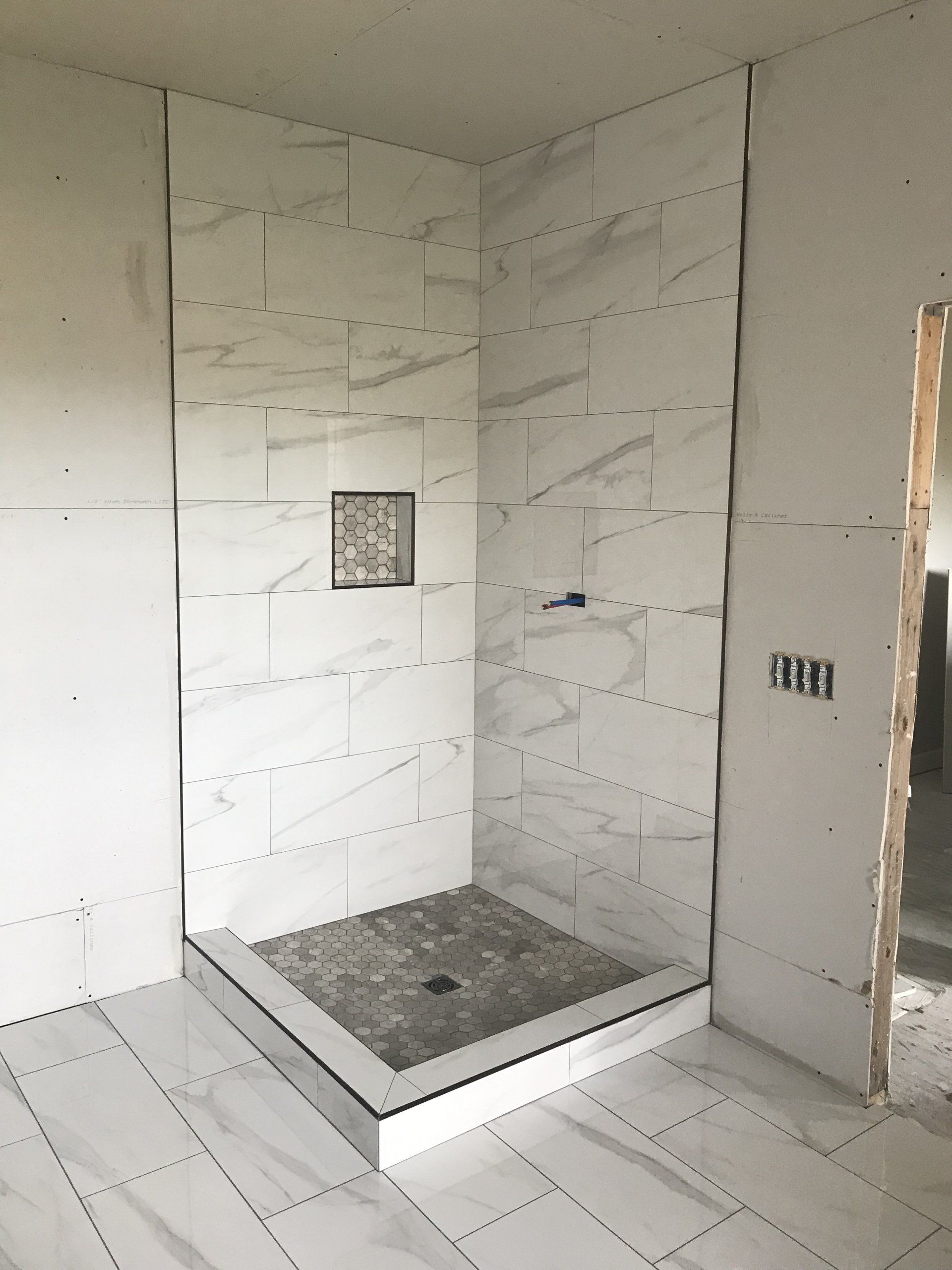 Bathroom under construction. White marble tiled shower with pebble floor, gray accent tile.
