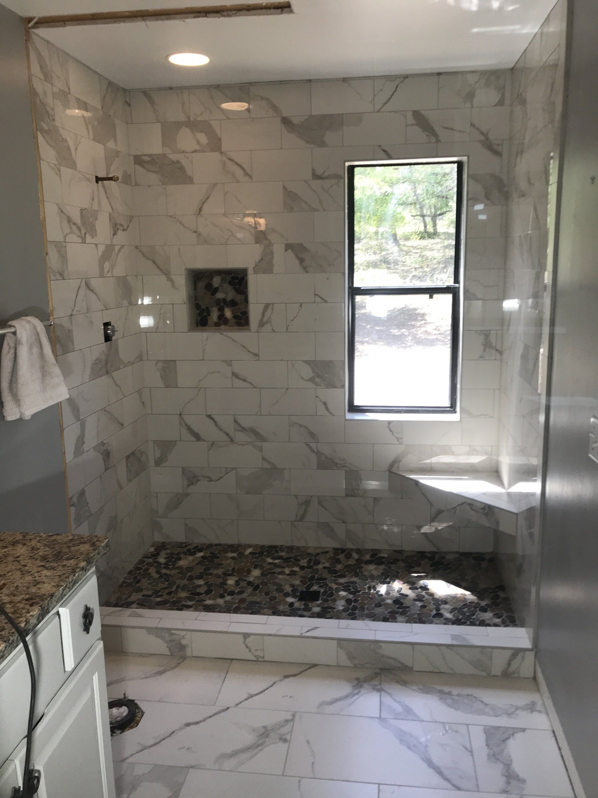 Bathroom with marble-look tile shower, pebble floor, window, and built-in bench.