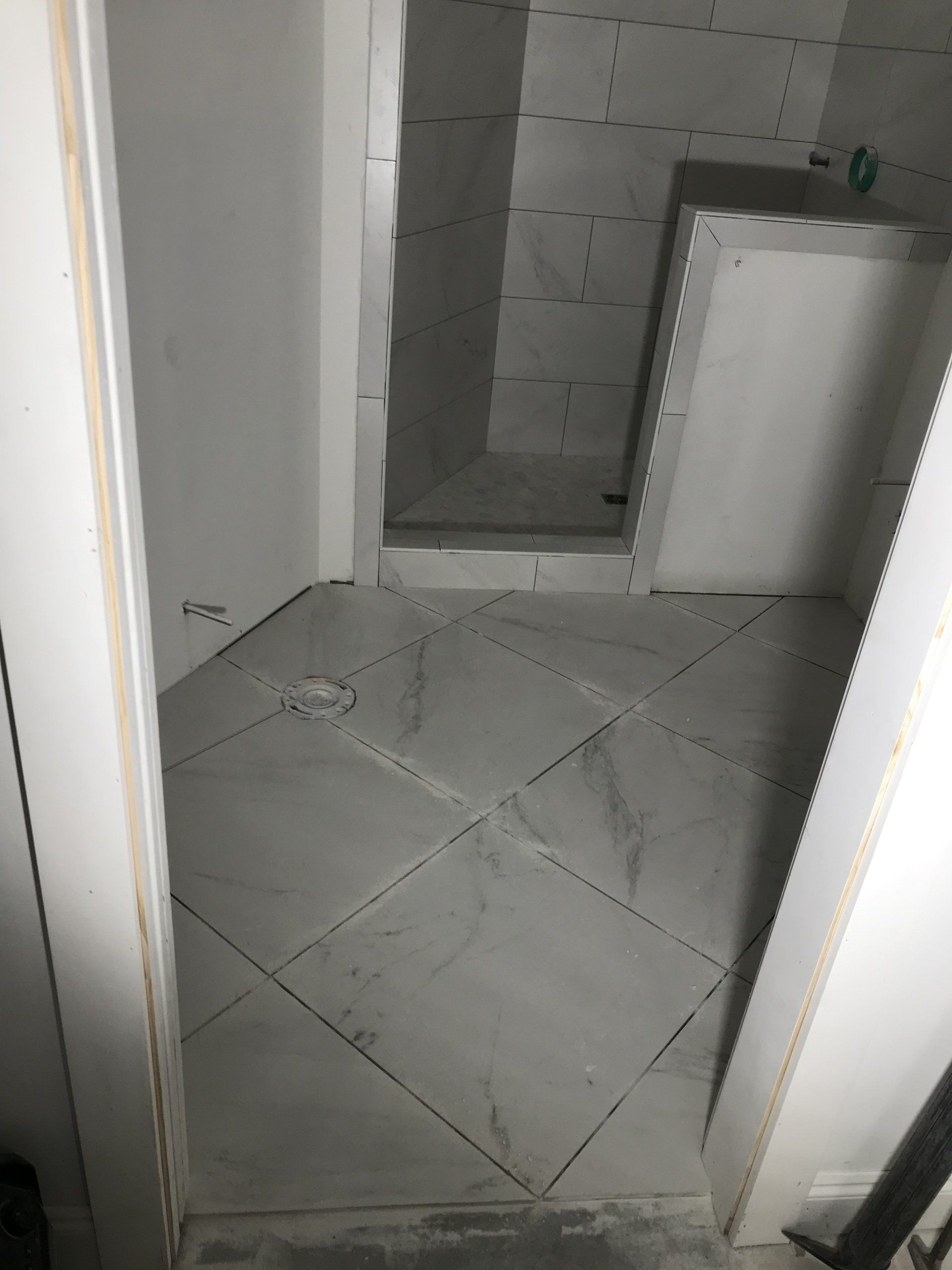 Bathroom under construction: grey tiled floor in a diamond pattern, shower area, walls with tile and white trim.