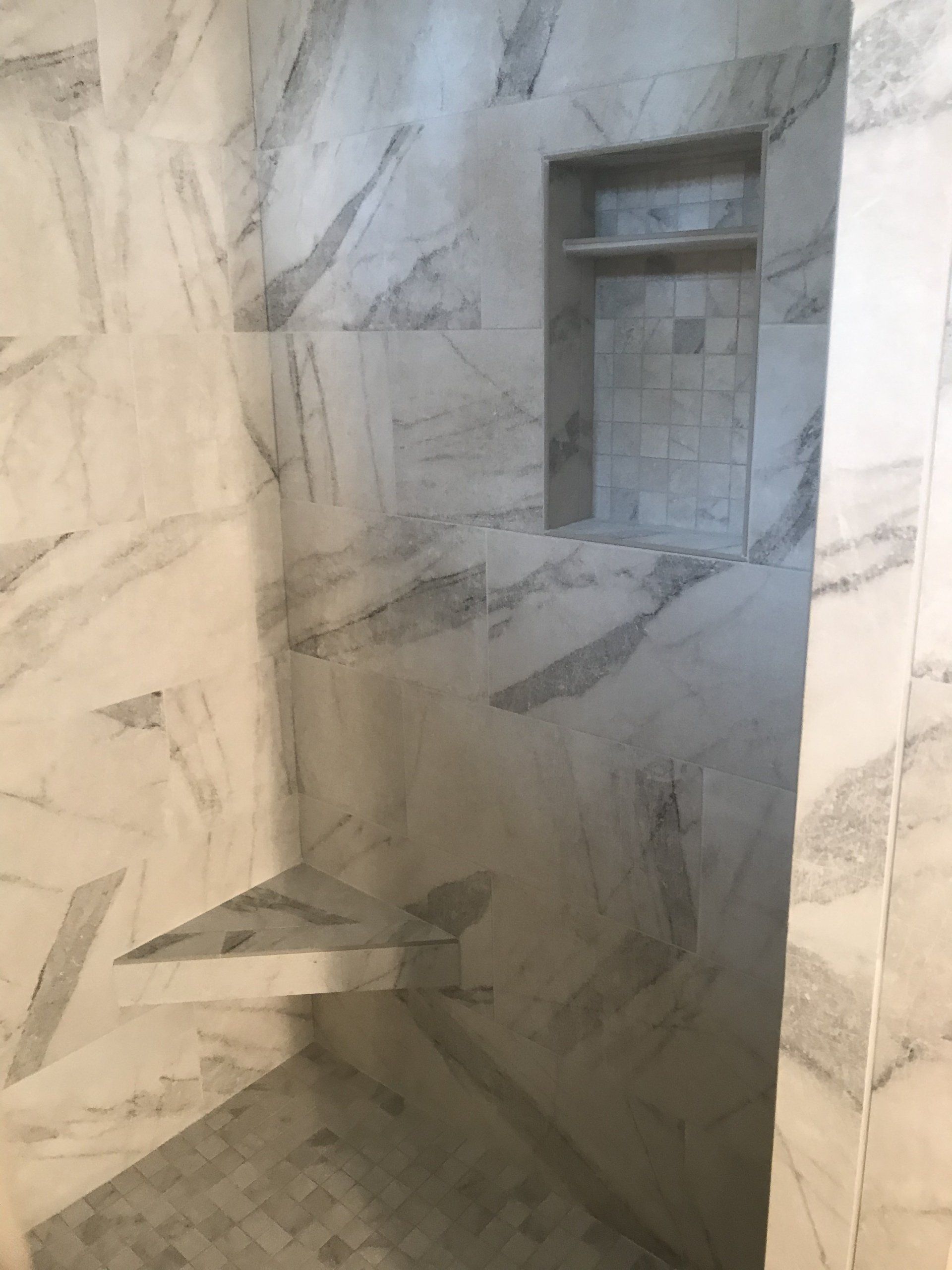 Shower with marble tiles, built-in shelves. Gray and white swirls, recessed storage, modern design.