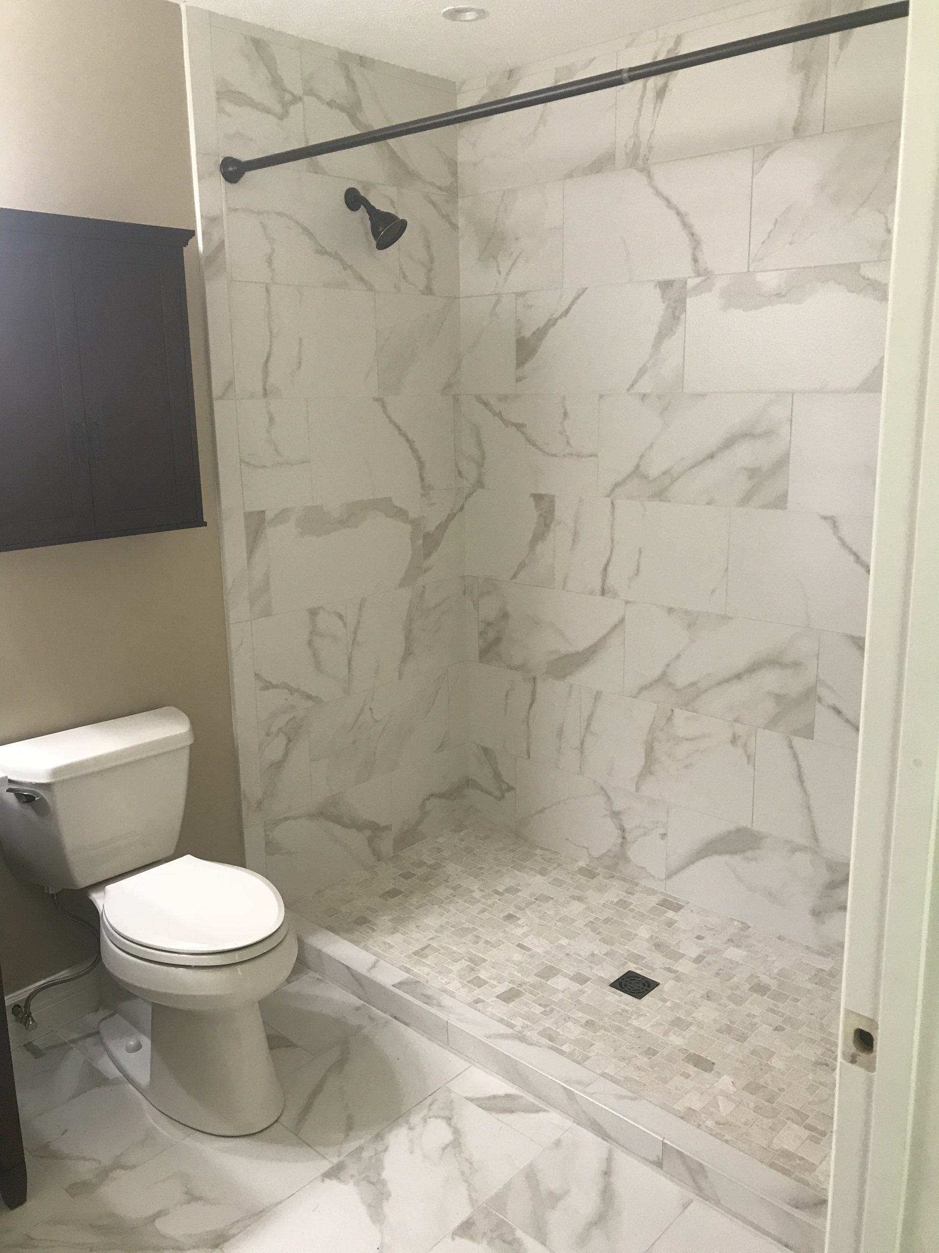 Bathroom with white marble tile shower and flooring, toilet, and a black shower rod.