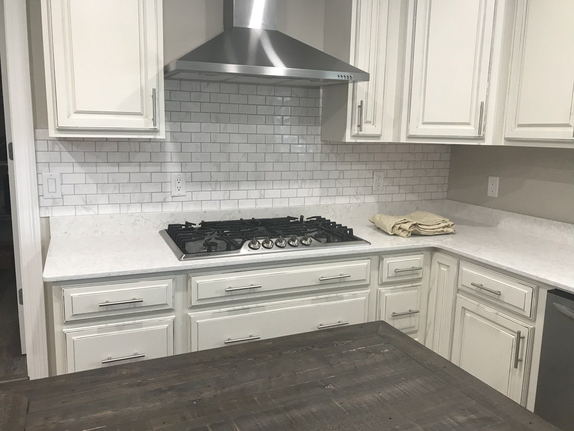 White kitchen with distressed cabinets, subway tile backsplash, and dark gas range.