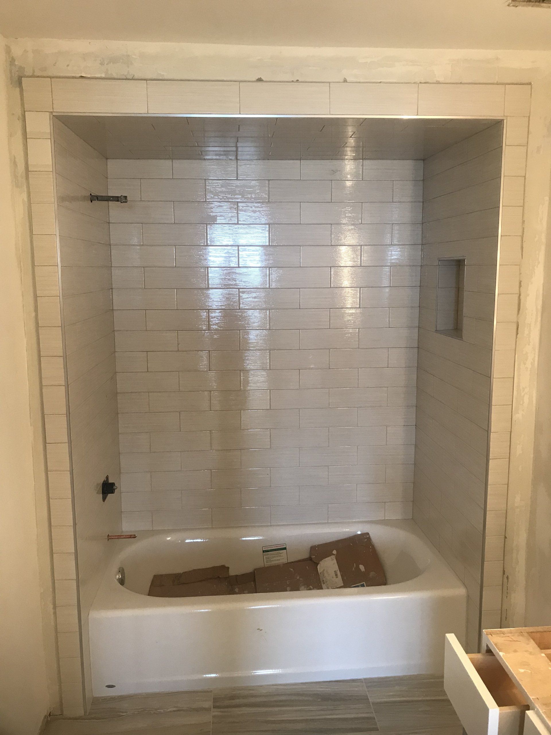 Bathtub alcove with white tiled walls, shower bar, and a recessed soap niche.