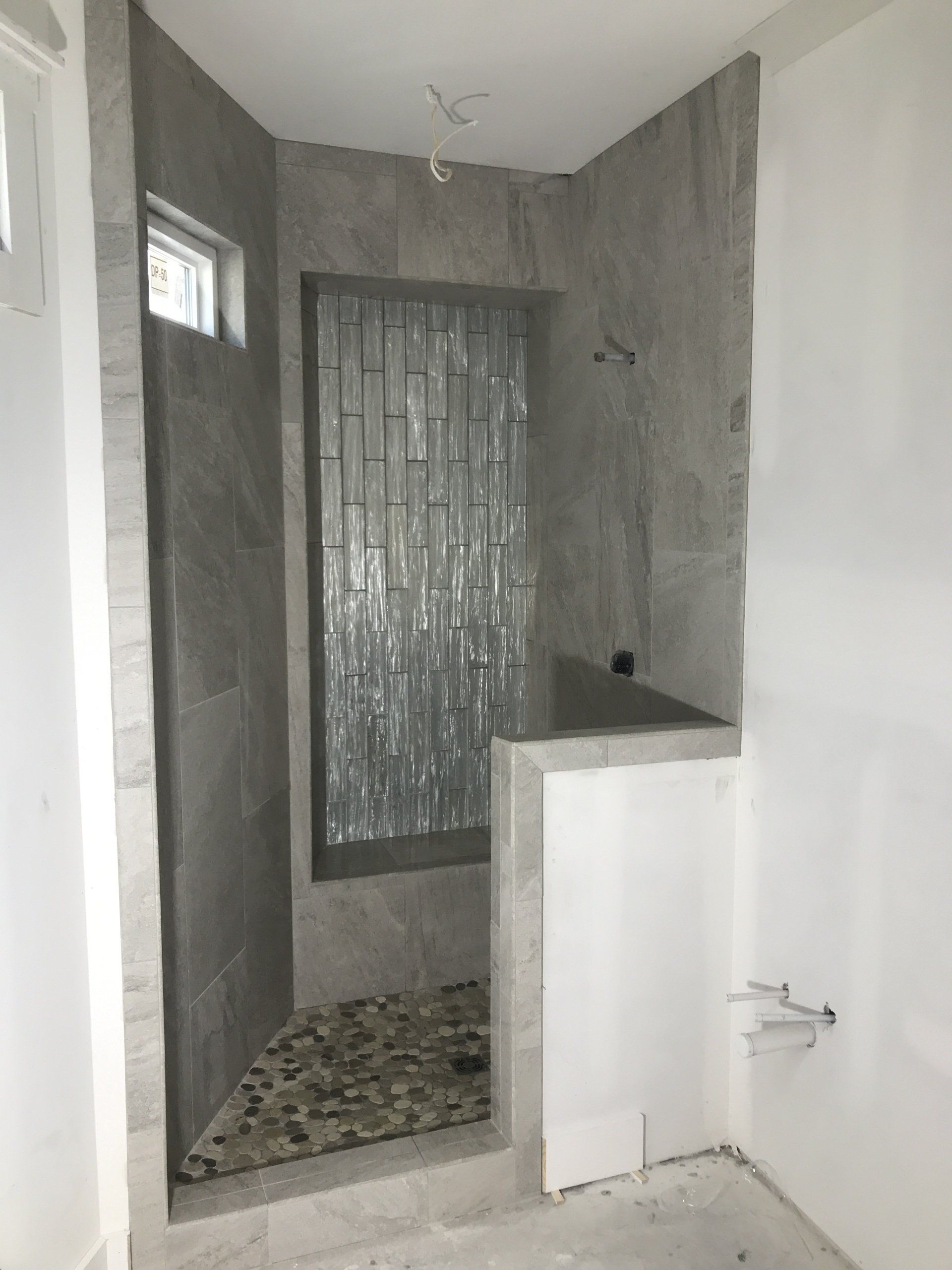 Shower under construction with pebble floor, gray tiled walls, and glass block window.