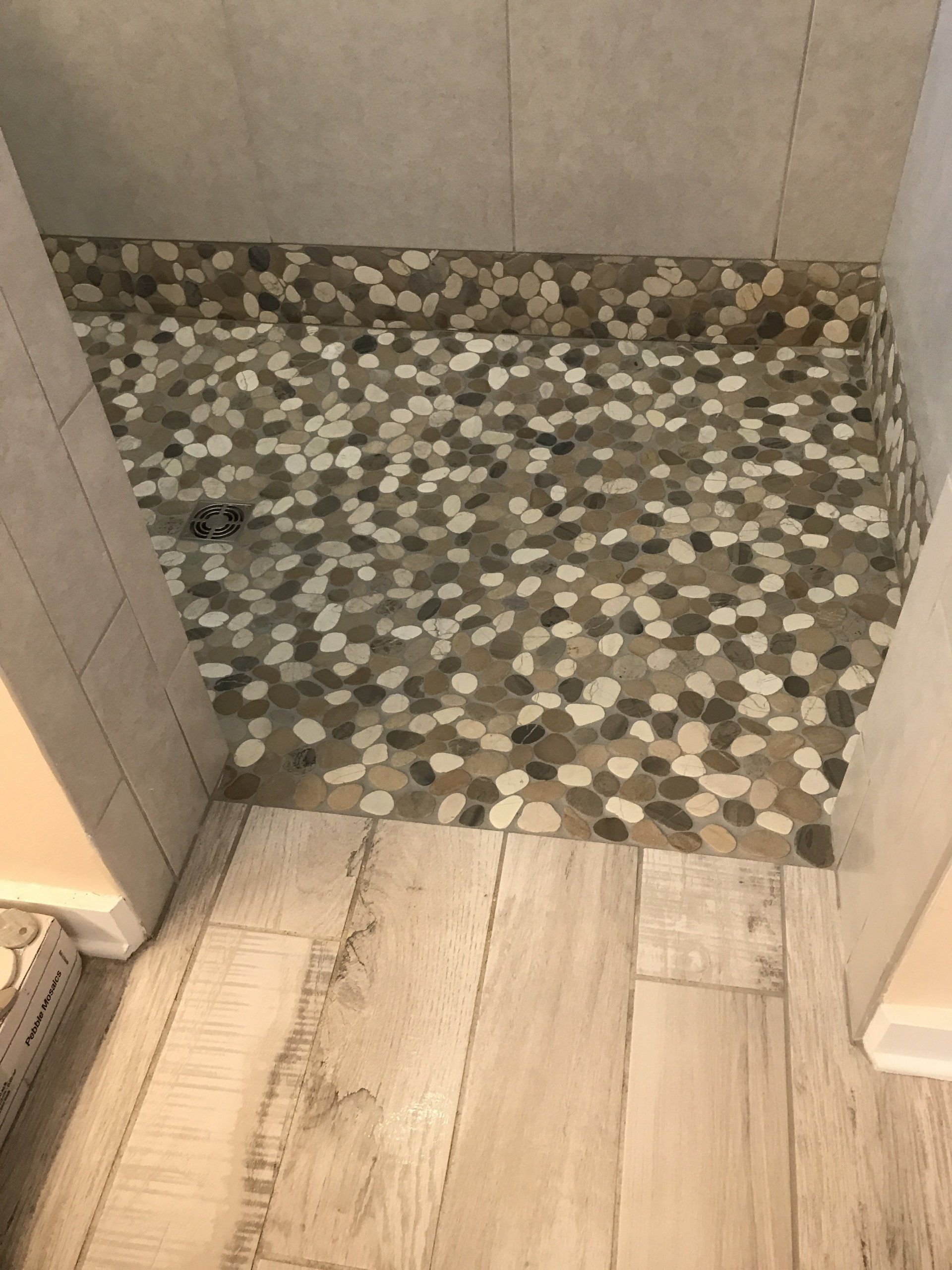 Shower with pebble floor, beige tile walls, and light wood-look flooring outside the shower.