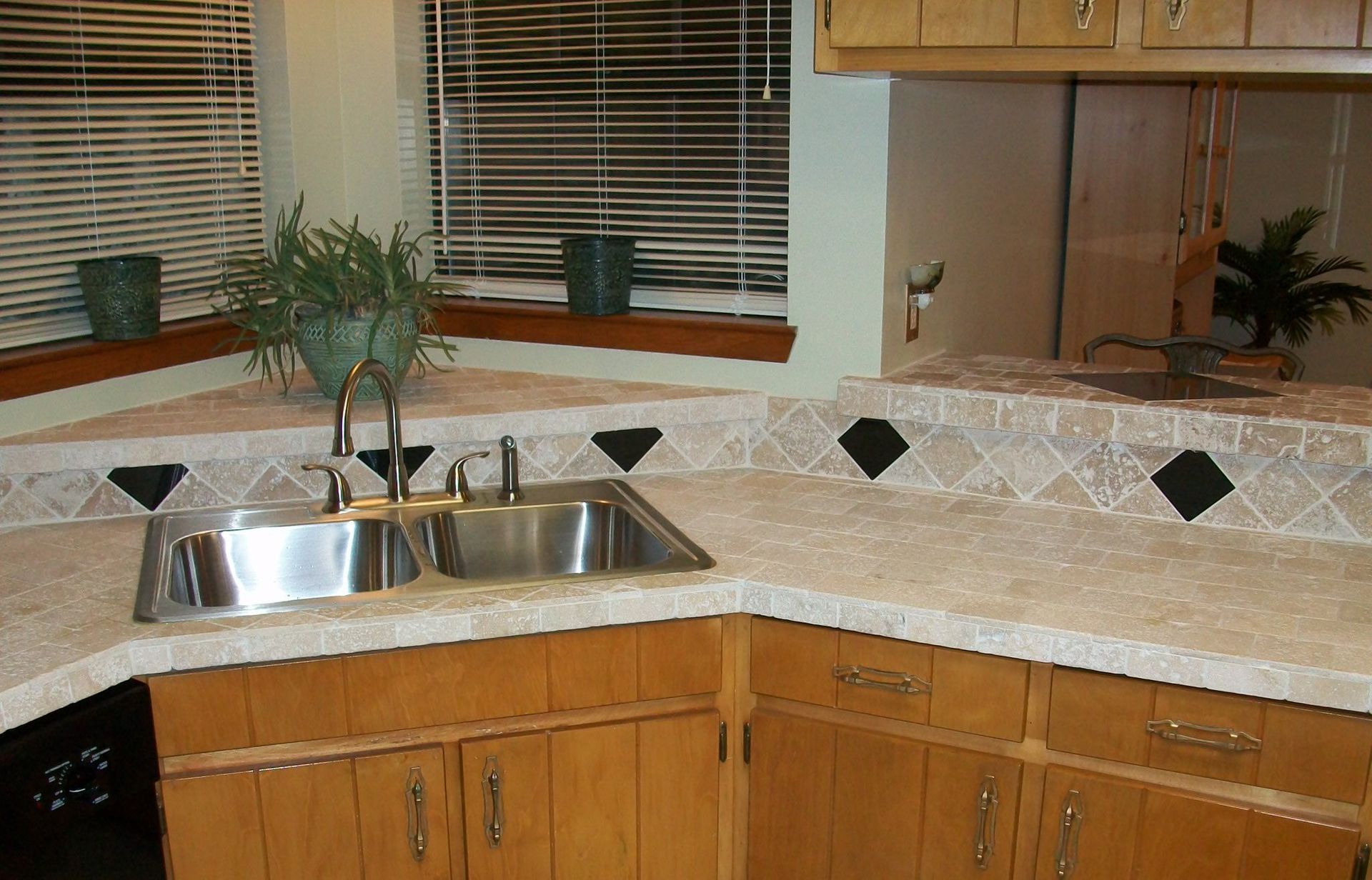 Kitchen with wood cabinets, tan countertops, stainless steel sink, and window with blinds.