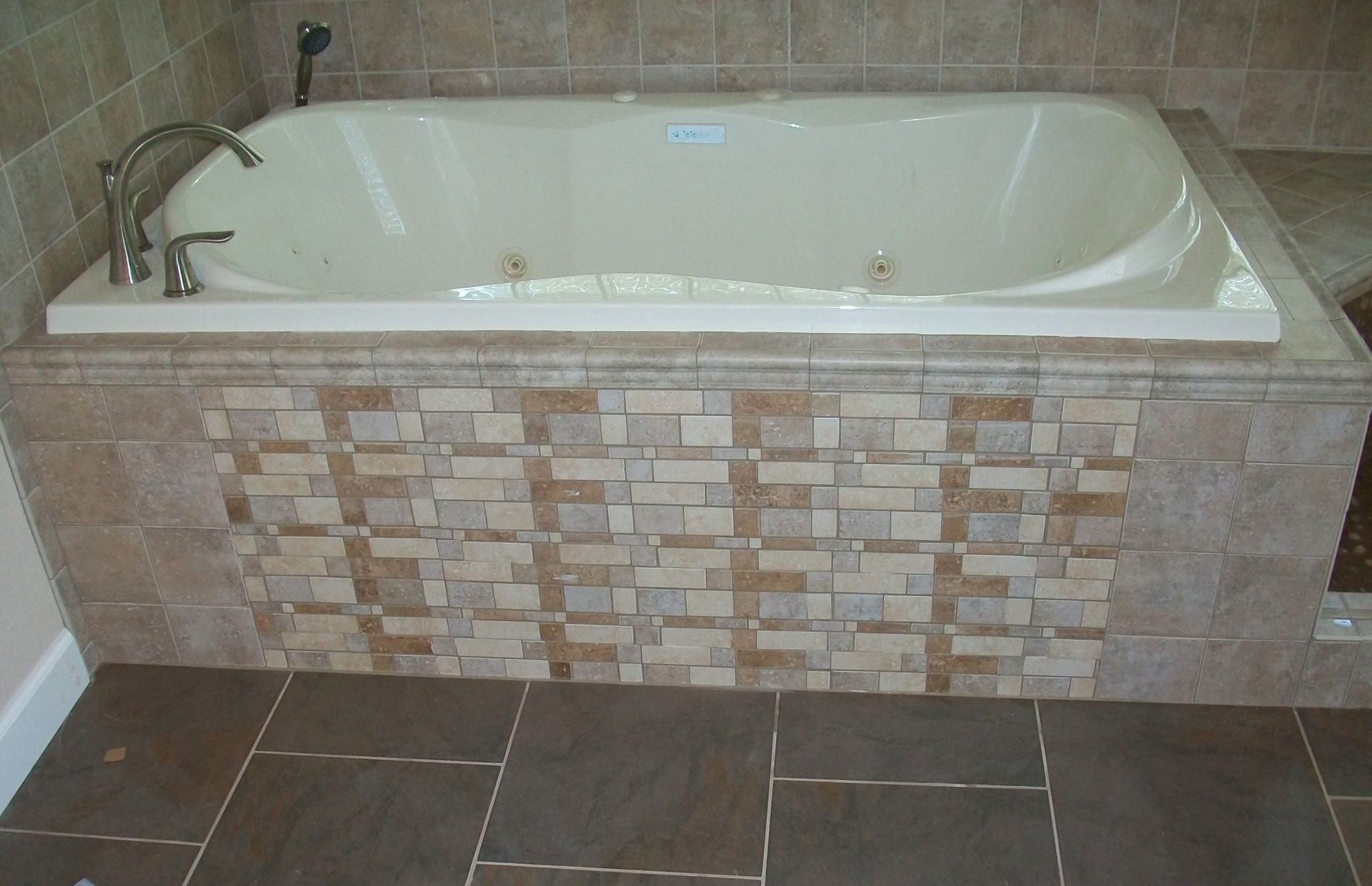 Bathtub with tile surround, brown floor and beige wall tiles.