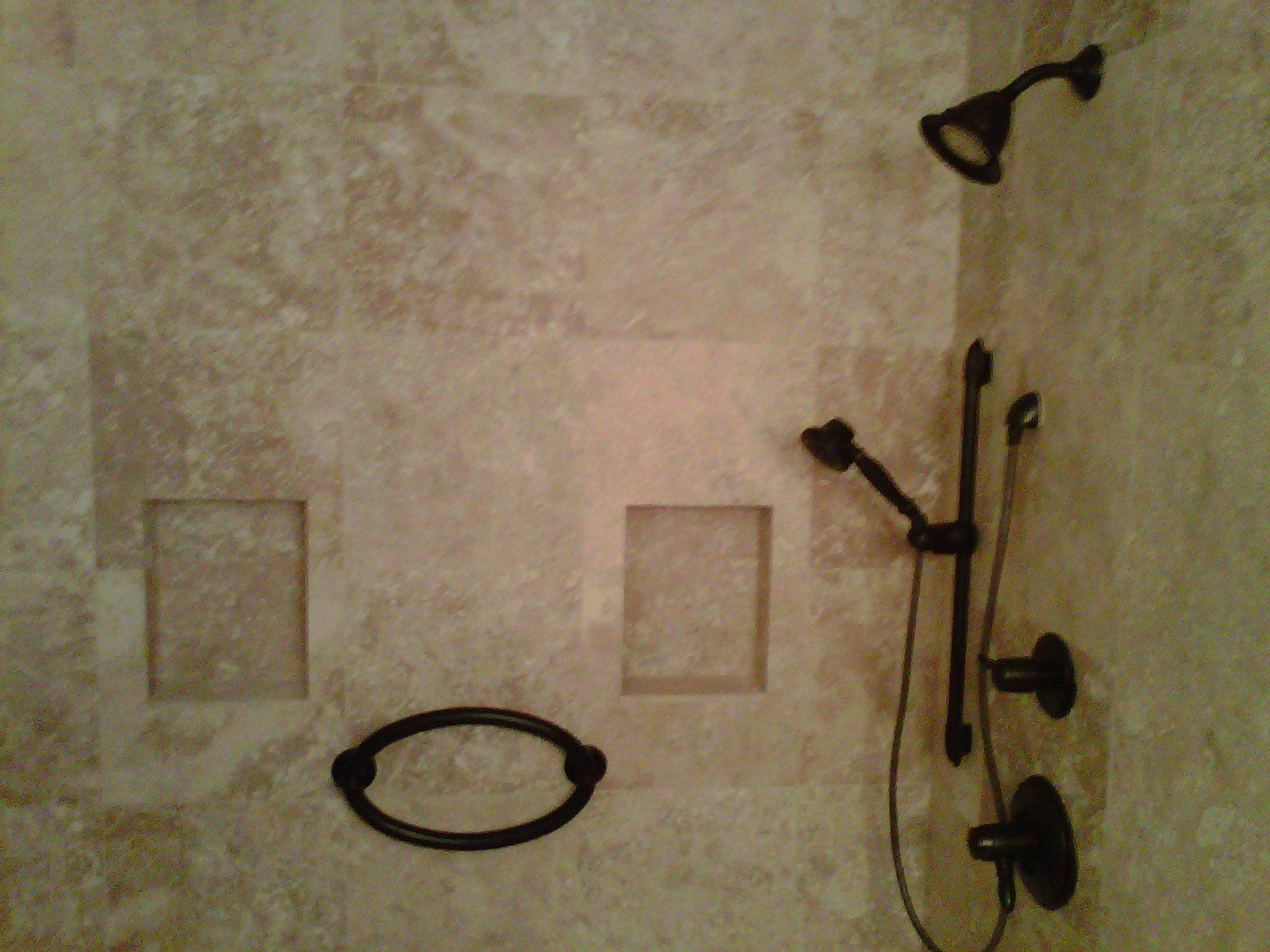 Shower with light brown tile, dark fixtures, two recessed shelves, and an oval towel ring.