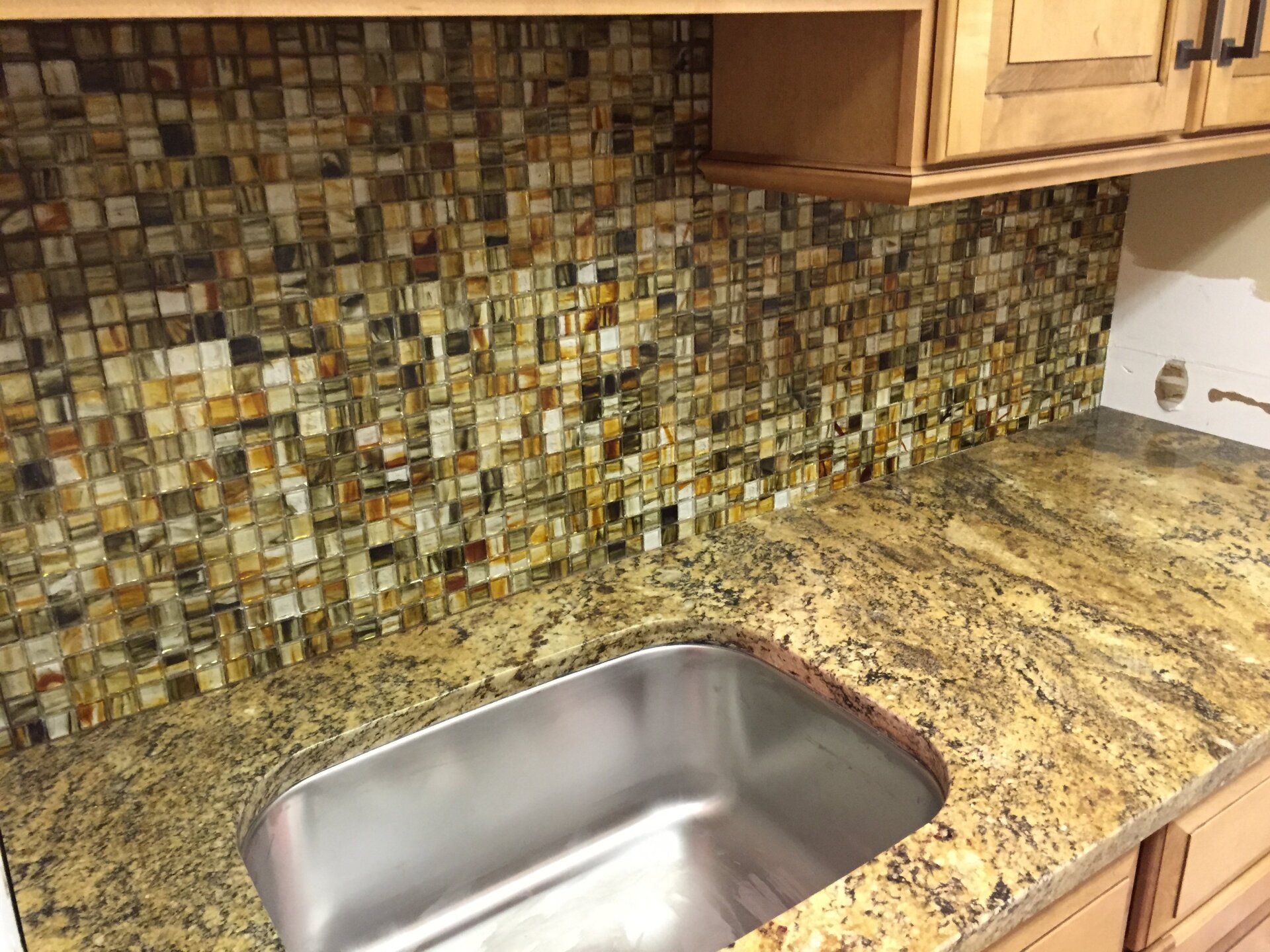 Kitchen with granite countertop, stainless steel sink, and mosaic tile backsplash; wood cabinets.