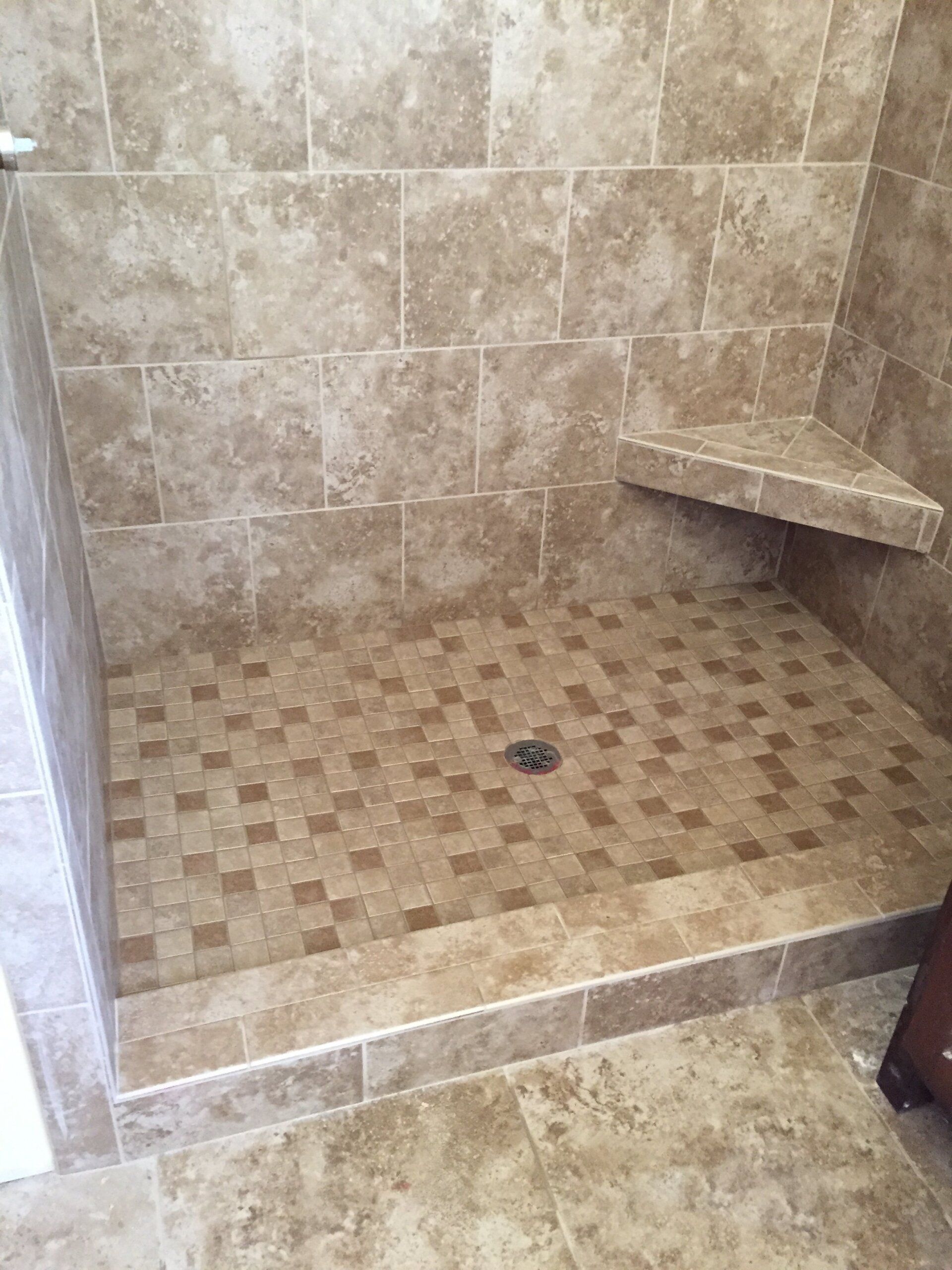 Tiled shower with corner seat. Brown and beige tiles cover walls and floor, with a drain in the center.